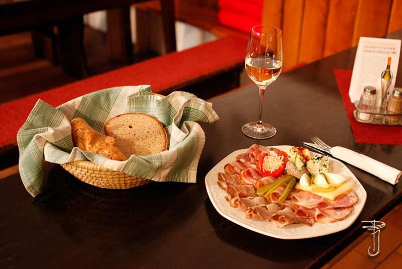 Ein gedeckter Tisch mit einer Wurstplatte, einem Brotkorb und einem Glas Weißwein.