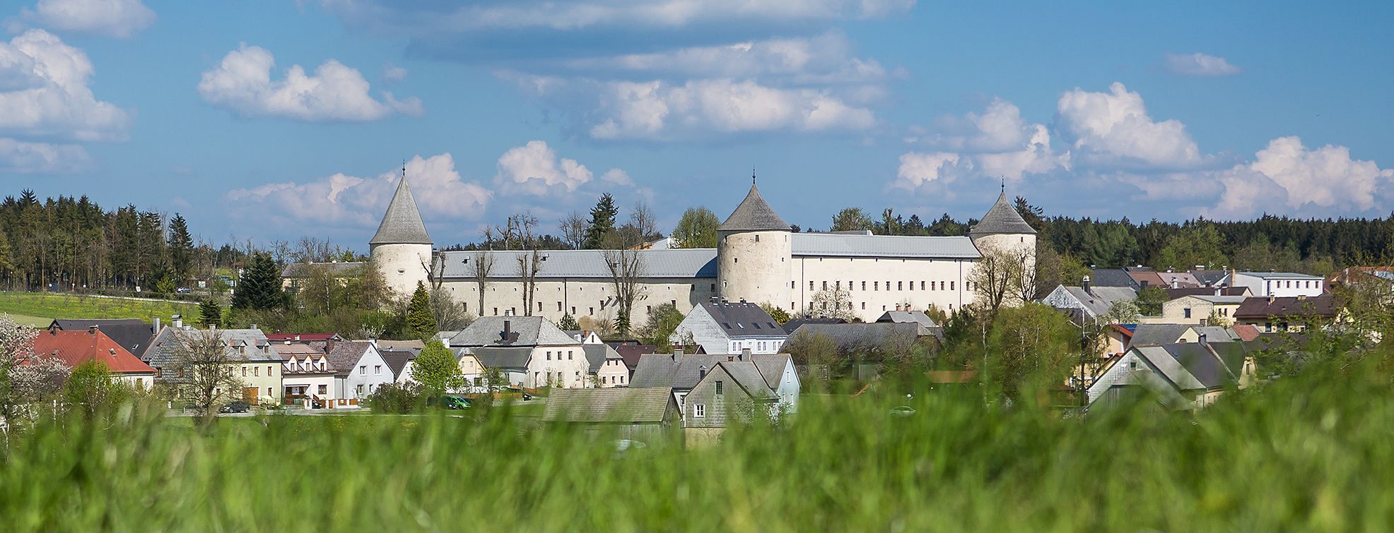 Schloss Ottenschlag in einer ländlichen Umgebung mit blühenden Bäumen und einem klaren blauen Himmel.