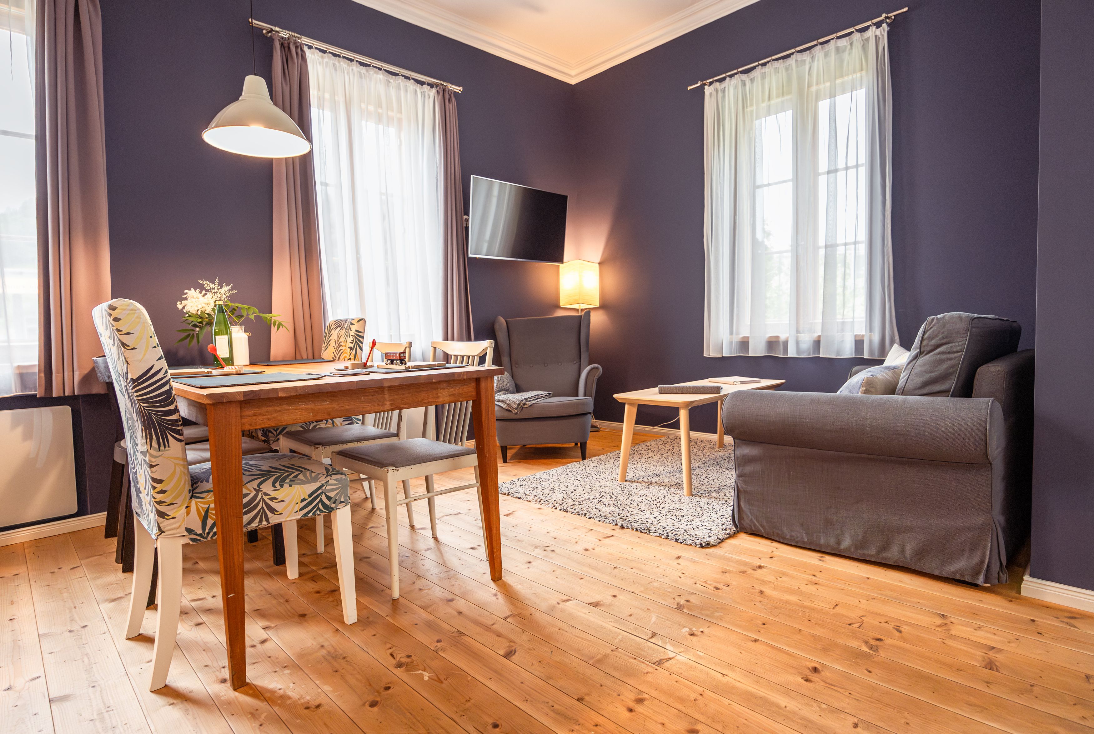 Gemütliches Wohnzimmer mit Holzboden, Esstisch, Stühlen, Sessel und Sofa.