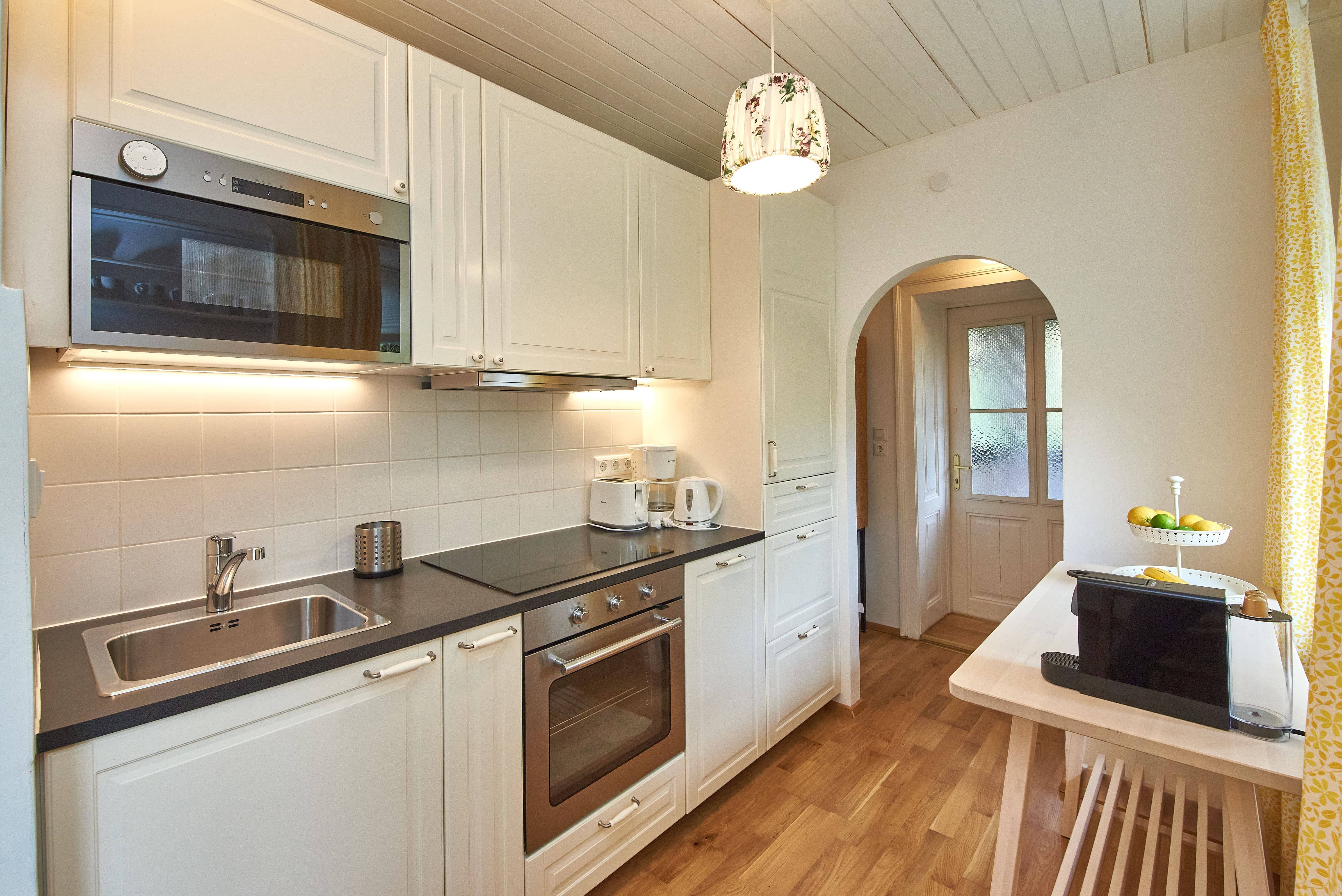 Moderne Küche mit weißen Schränken, Holzfußboden und Geräten wie Ofen und Mikrowelle.