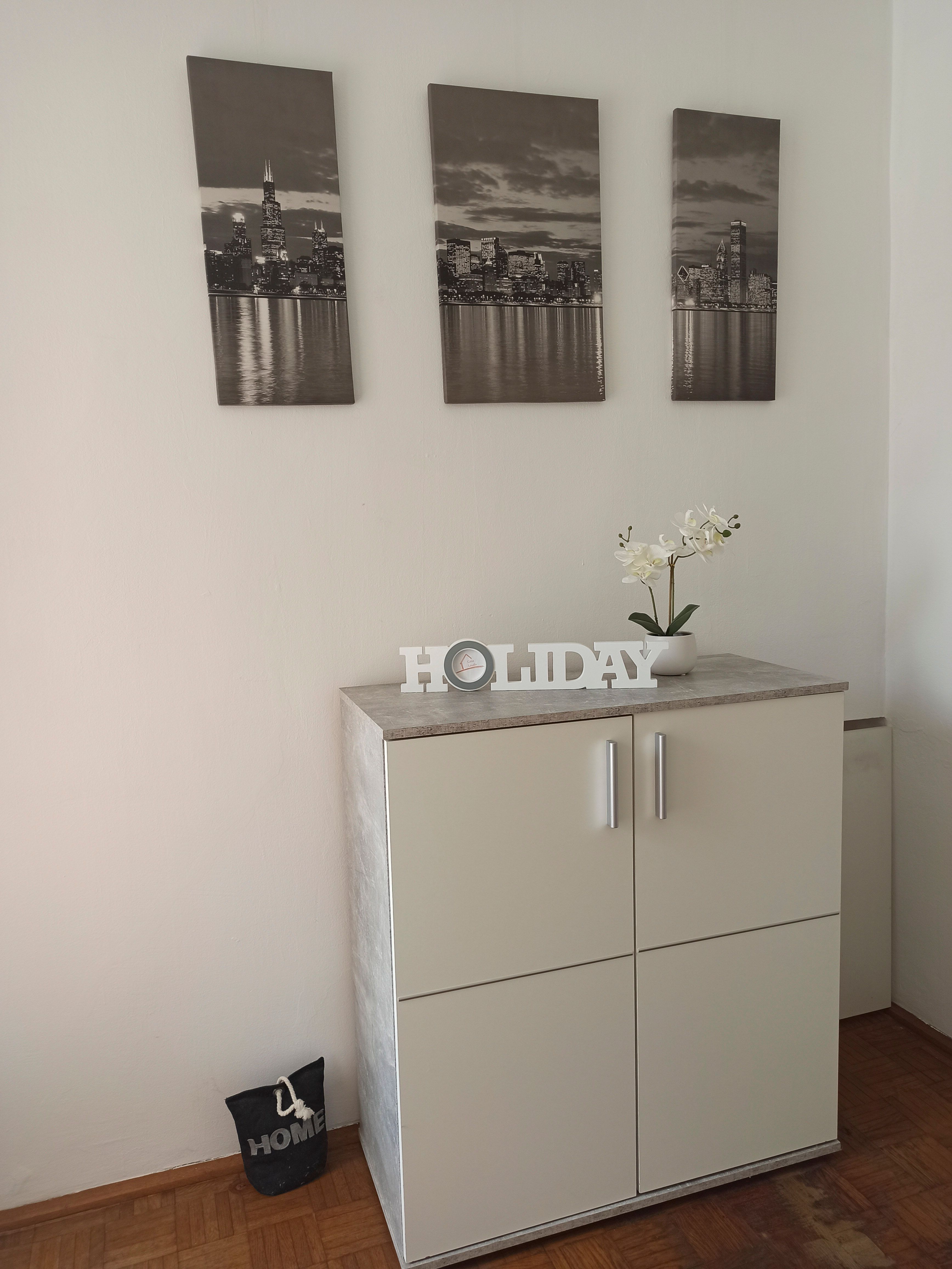 Ein weißer Schrank mit Dekoration und drei Stadtbildern an der Wand.