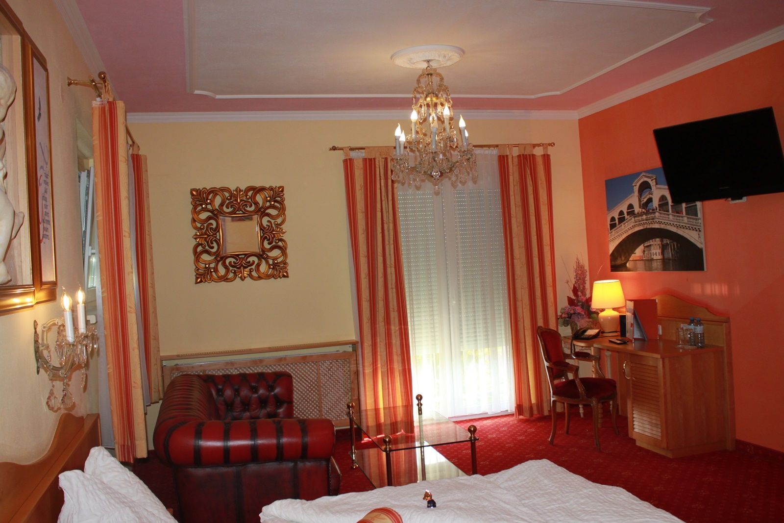 Elegantes Hotelzimmer mit Kronleuchter, Ledersofa, Schreibtisch und großem Fenster mit Vorhängen.