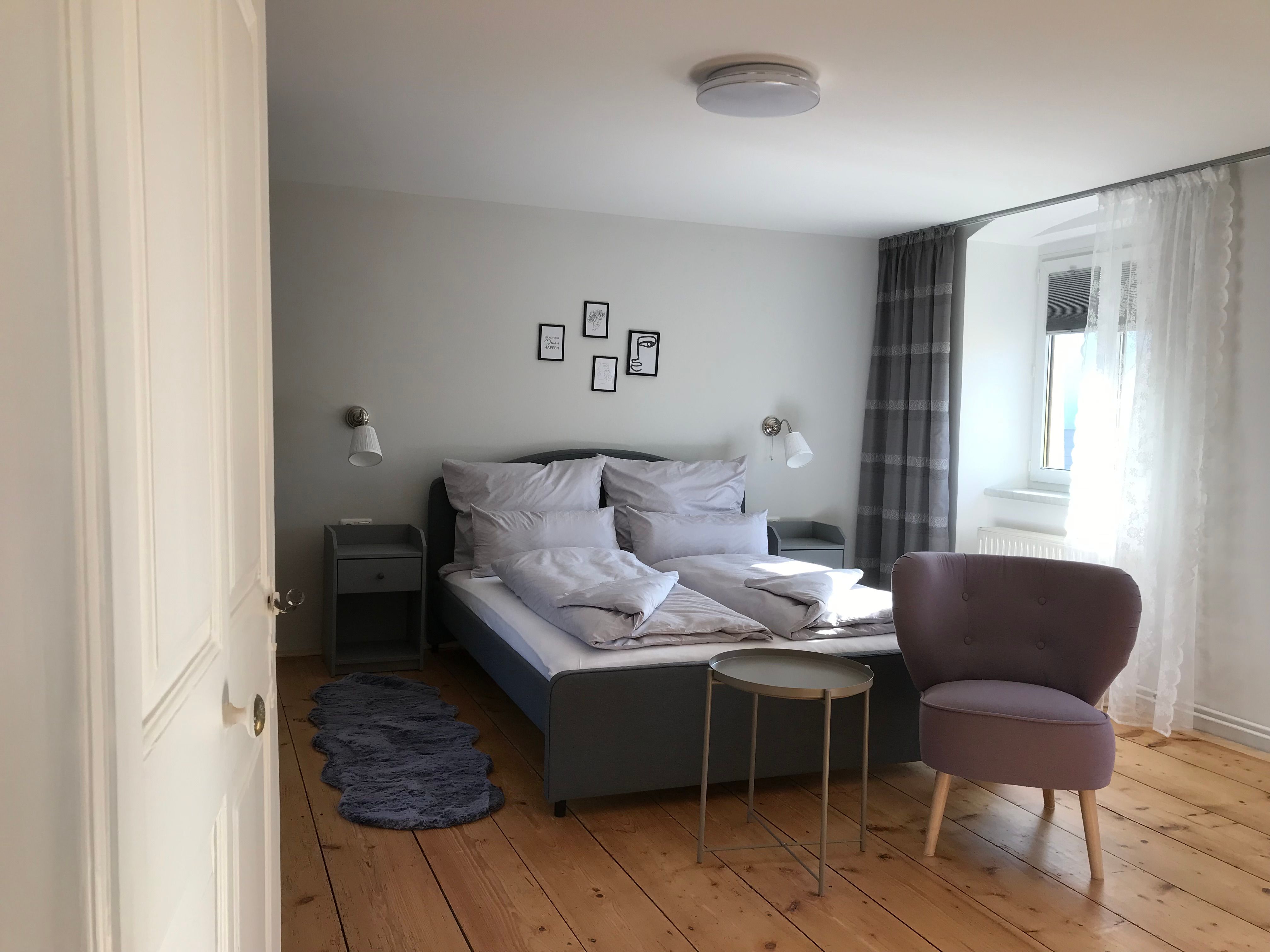 Modern eingerichtetes Doppelzimmer mit Bett, Sessel und kleinem Tisch auf Holzboden.