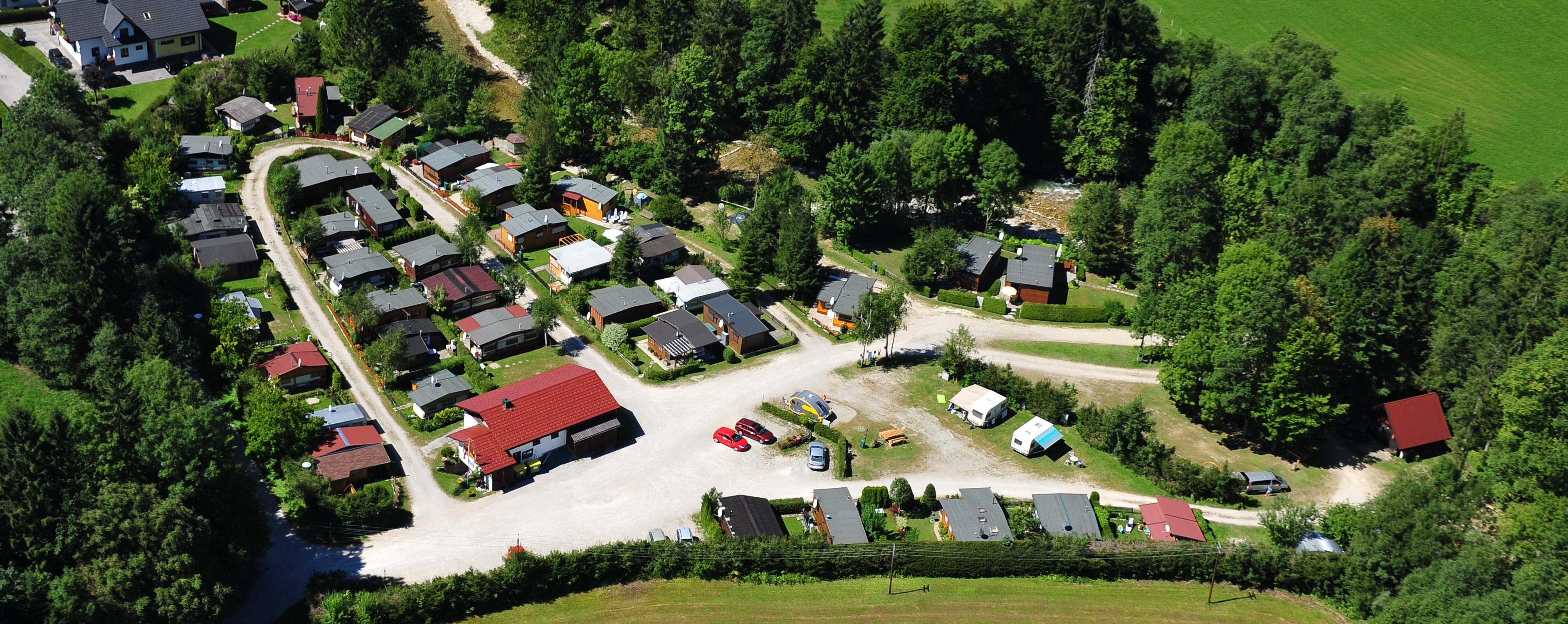 Luftaufnahme eines Campingplatzes mit Wohnwagen und kleinen Häusern, umgeben von Bäumen und Wiesen.