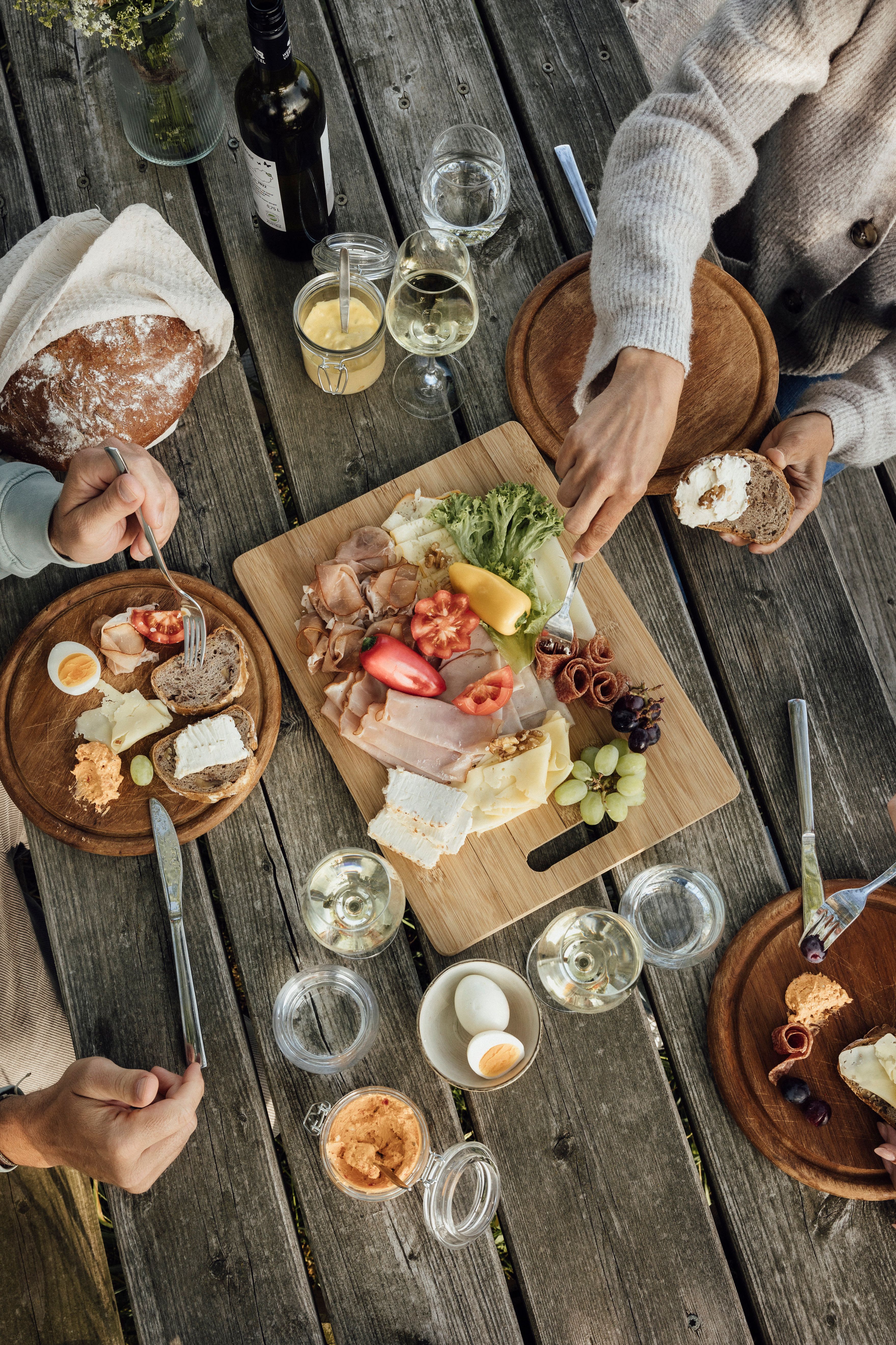Ein rustikaler Holztisch mit einer Jause aus Brot, Käse, Aufschnitt, Gemüse und Wein.