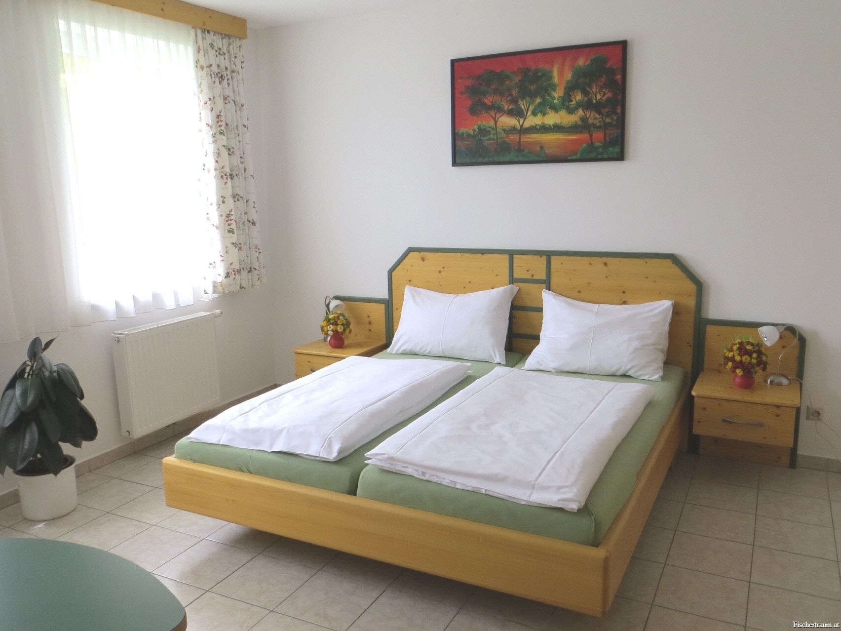 Ein Gästezimmer mit Doppelbett, Nachttischen, einem Bild an der Wand und einem Fenster mit Vorhängen.