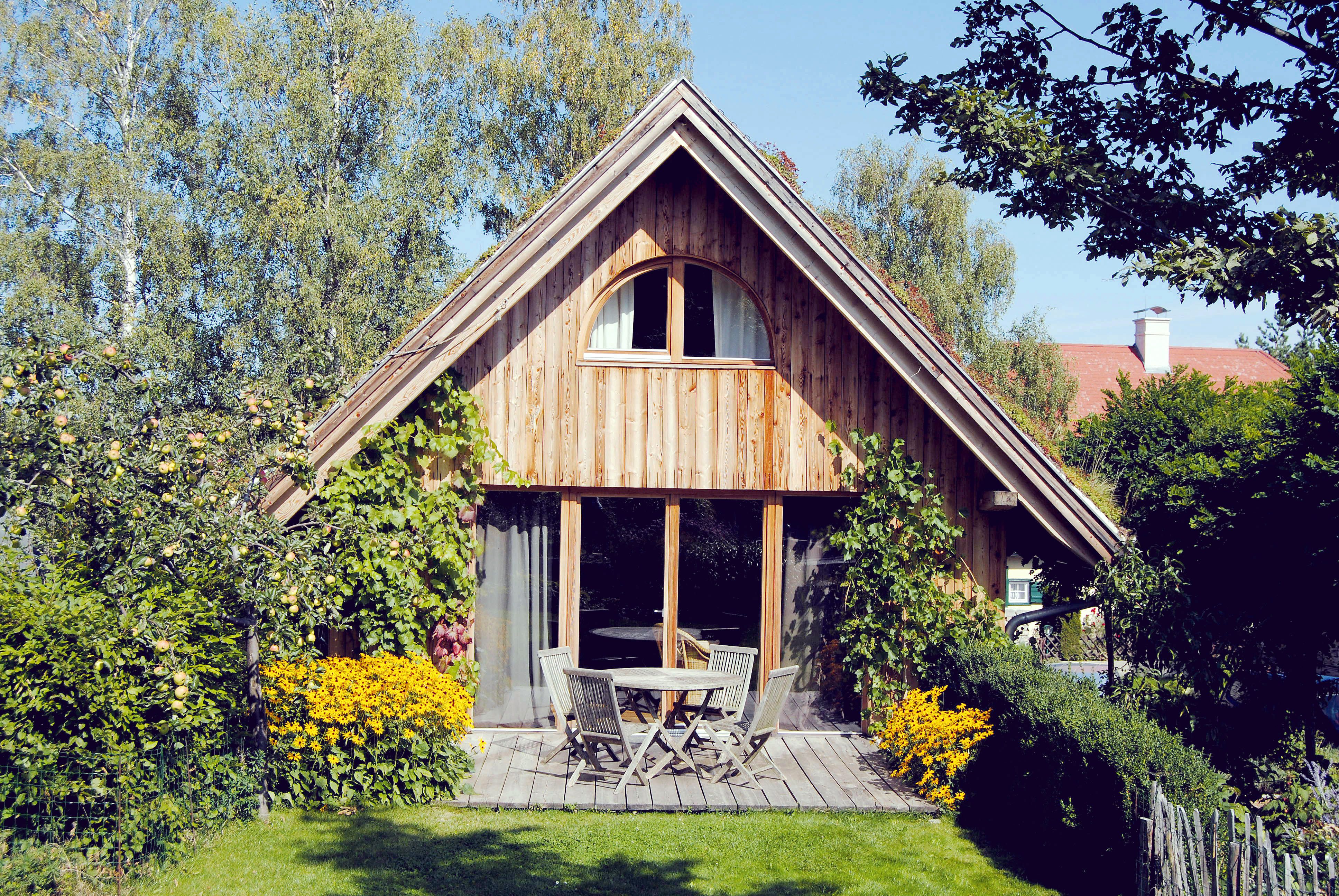 Ein gemütliches Holzferienhaus mit Terrasse, umgeben von Bäumen und Blumen.