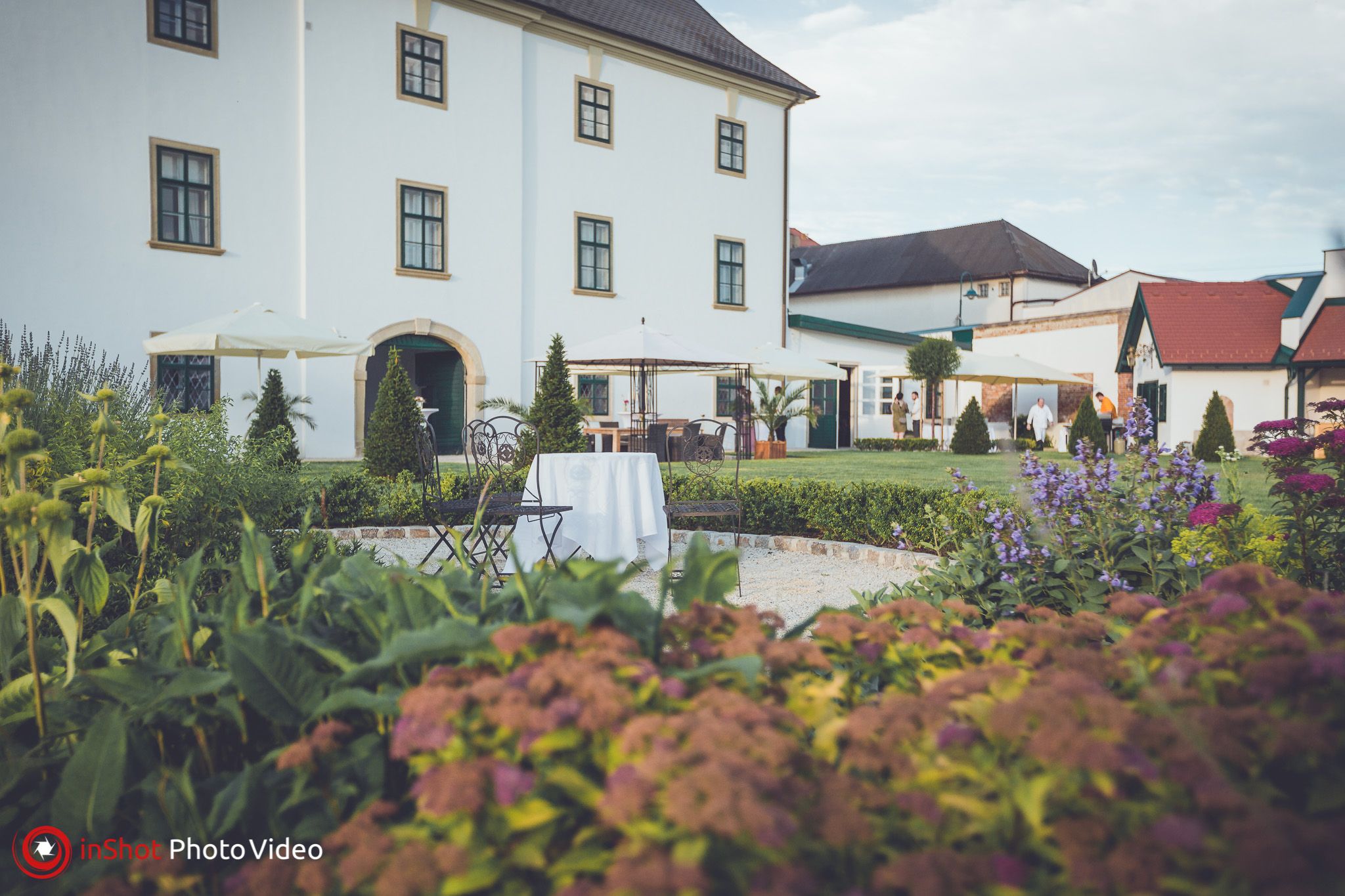 Gartenansicht von Schloss Raggendorf mit Blumen, Tischen und Stühlen im Vordergrund.