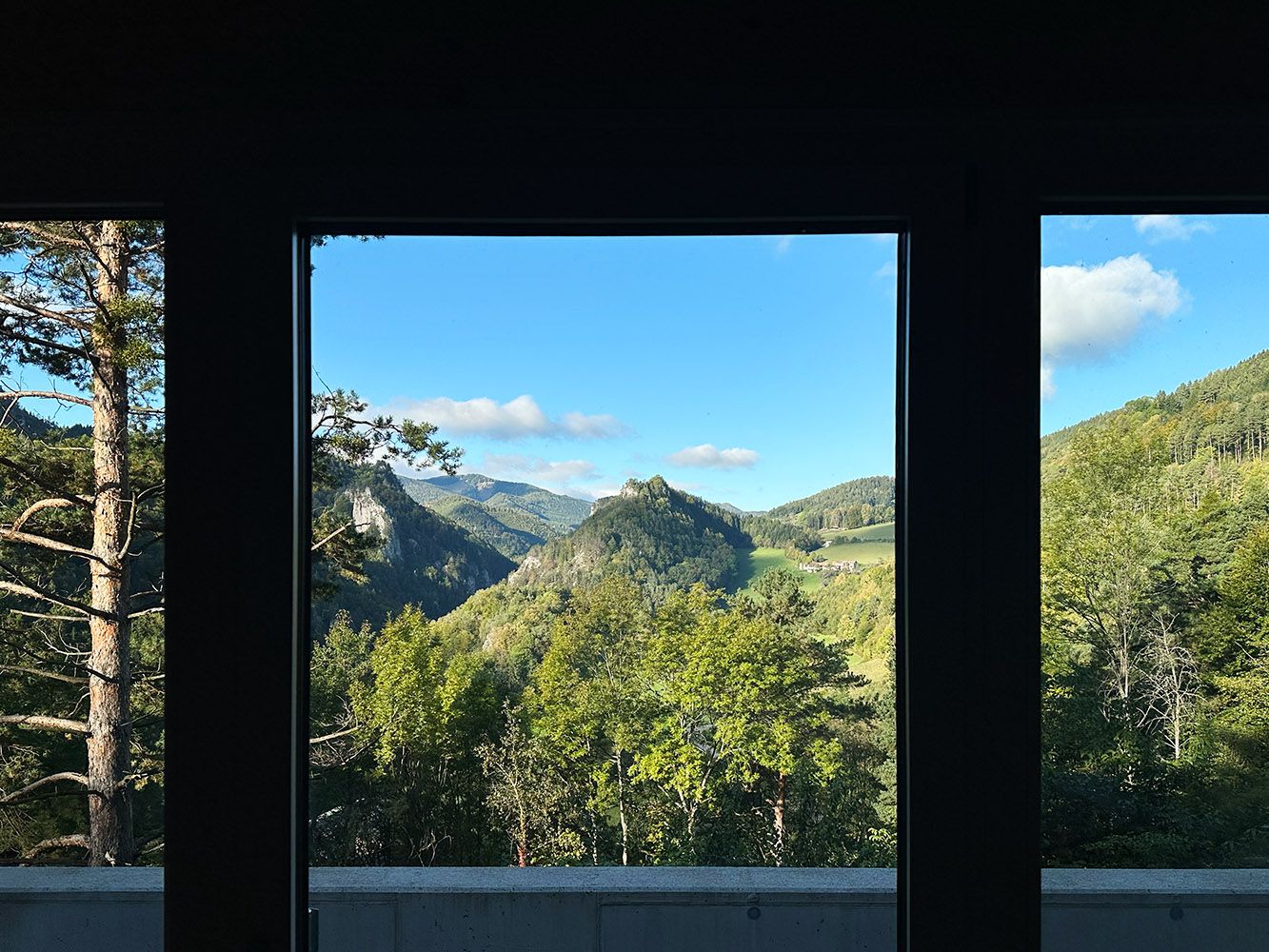 Blick aus einem Fenster auf eine grüne Berglandschaft mit blauem Himmel.