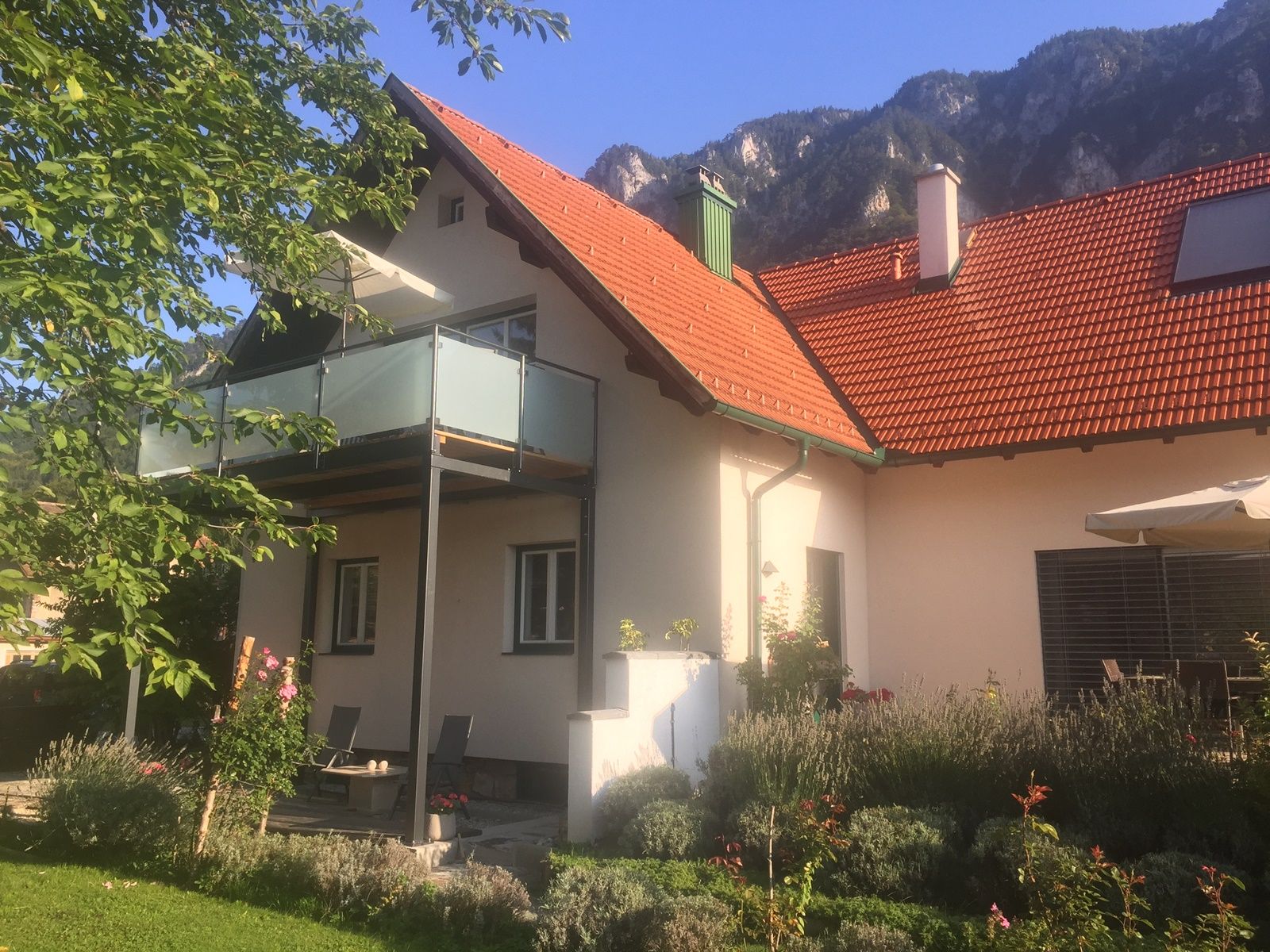 Ferienhaus mit Balkon und Garten vor Bergkulisse.