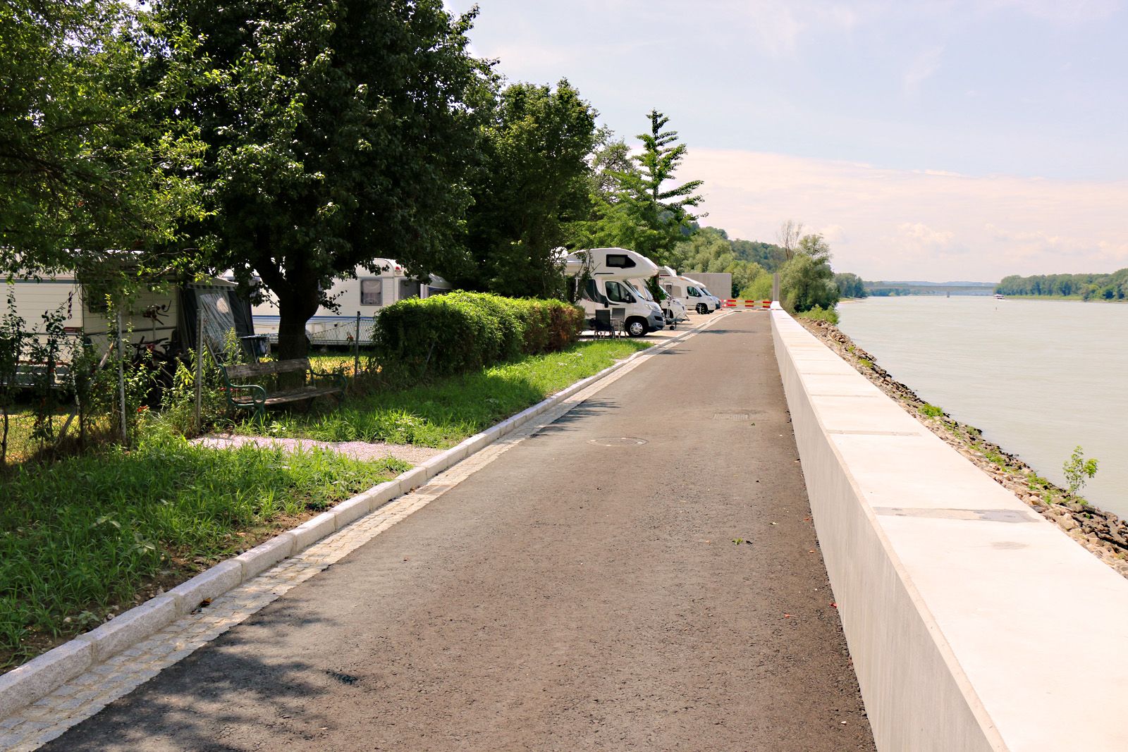 Wohnmobile parken entlang eines Weges an der Donau.