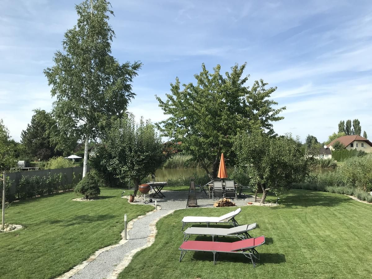Ein gepflegter Garten mit Rasen, Bäumen, Sonnenliegen und einem Tisch mit Sonnenschirm.