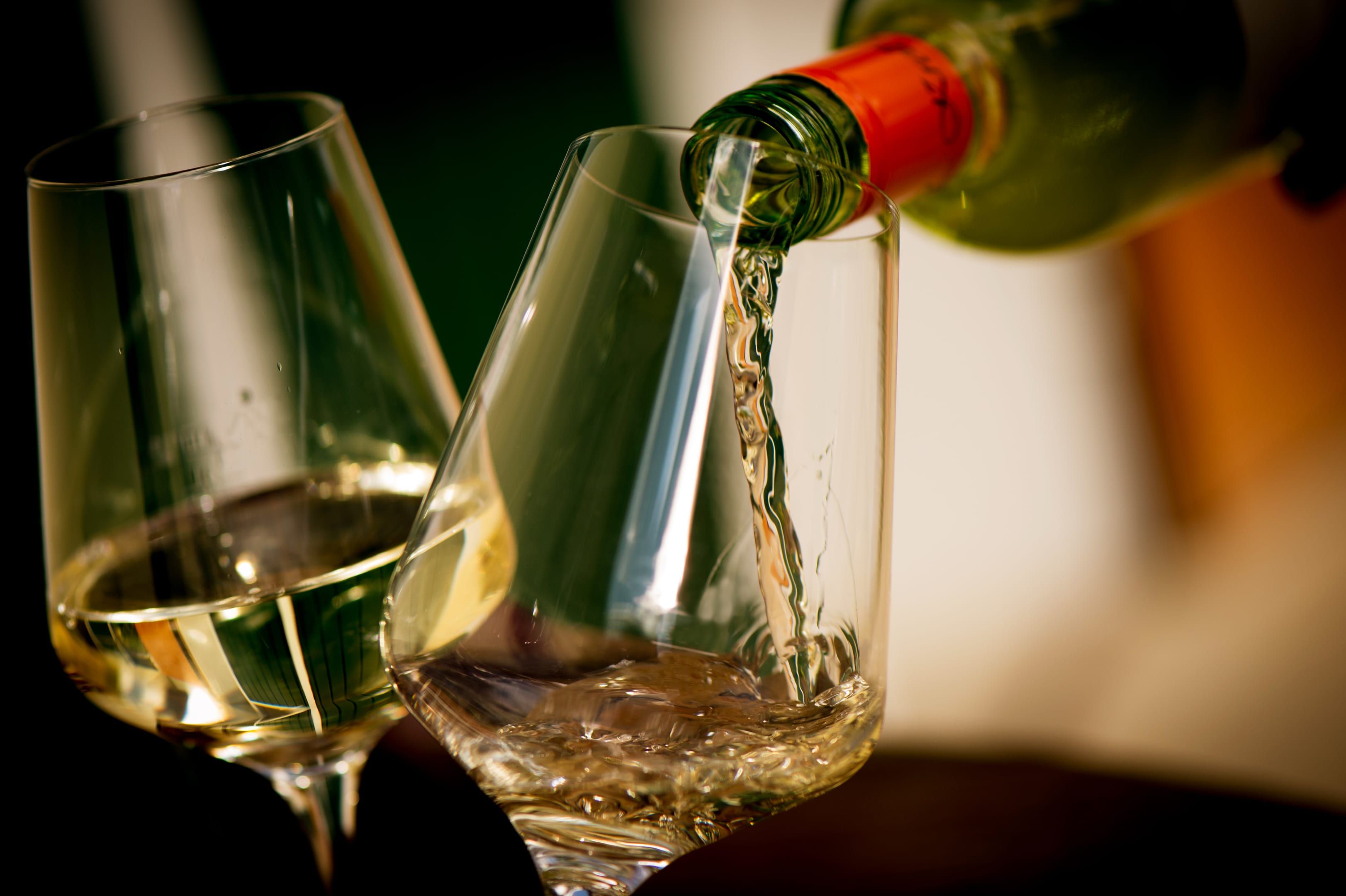 Weißwein wird in ein Glas eingeschenkt, daneben ein weiteres gefülltes Glas.