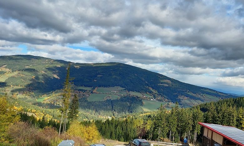Panoramablick auf eine hügelige Landschaft mit Wäldern und Feldern unter einem bewölkten Himmel.