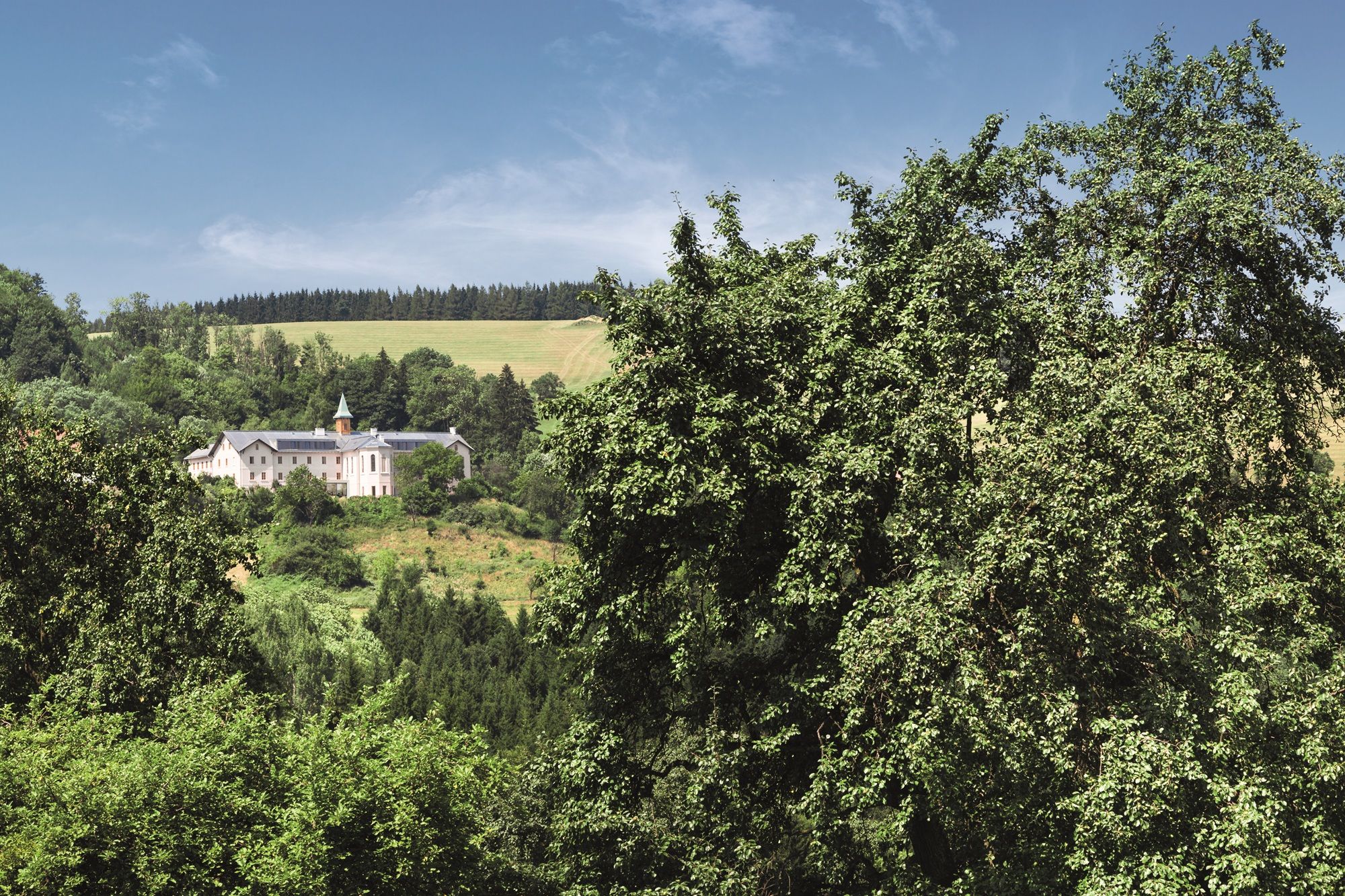 Ein Hotelgebäude inmitten einer grünen Landschaft mit Bäumen und Hügeln im Hintergrund.
