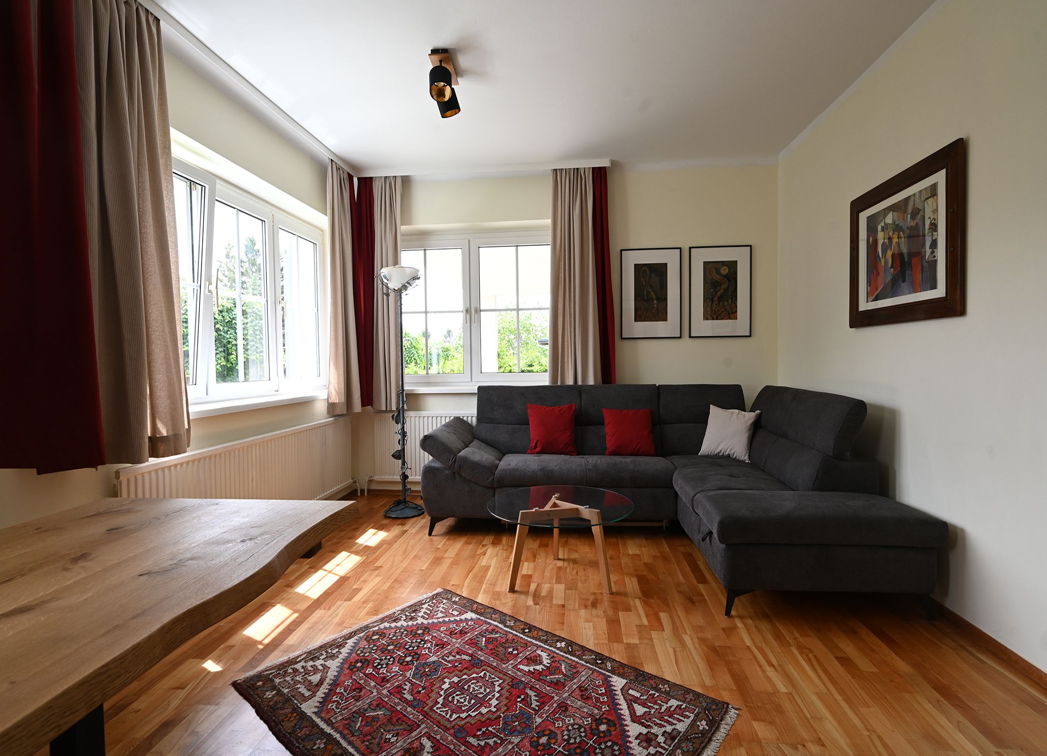 Modernes Wohnzimmer mit grauem Sofa, Holztisch, Teppich und großen Fenstern.
