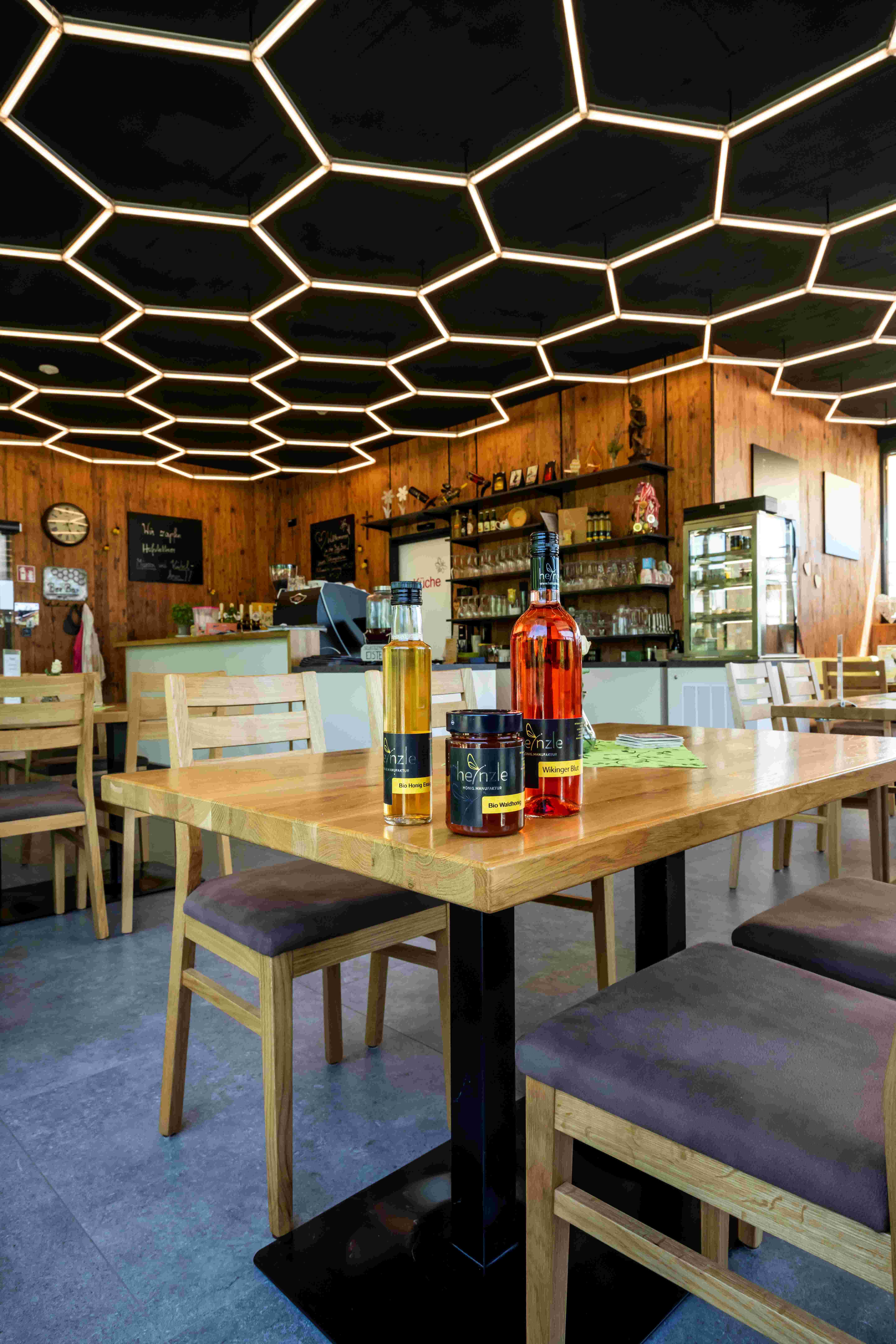 Innenansicht einer Bar mit honigförmiger Deckenbeleuchtung und Honigprodukten auf einem Tisch.