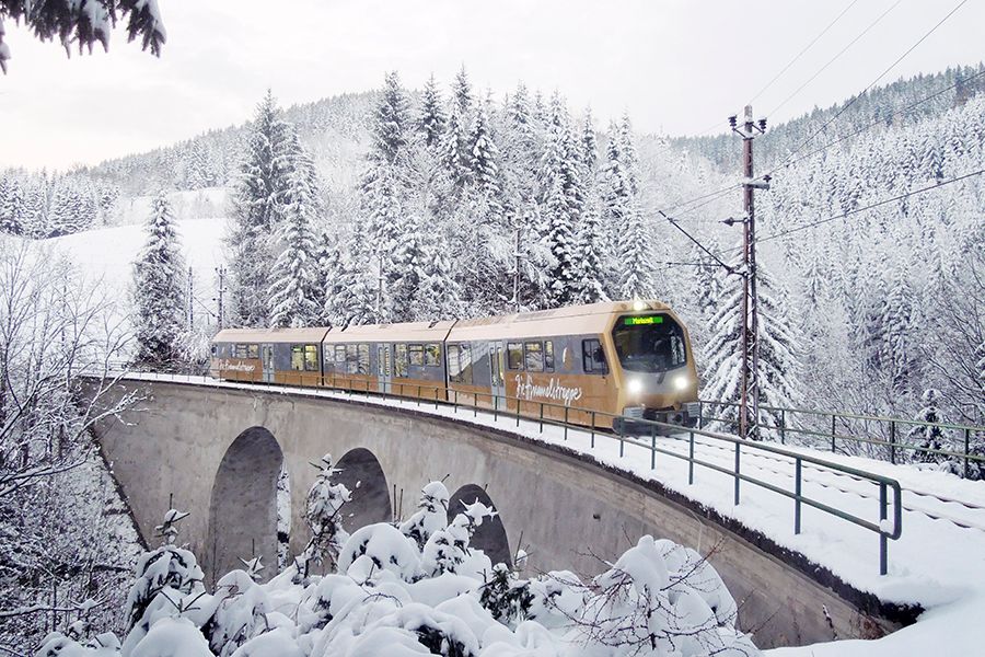 Garnitur der Mariazellerbahn fährt durch eine verschneite Landschaft