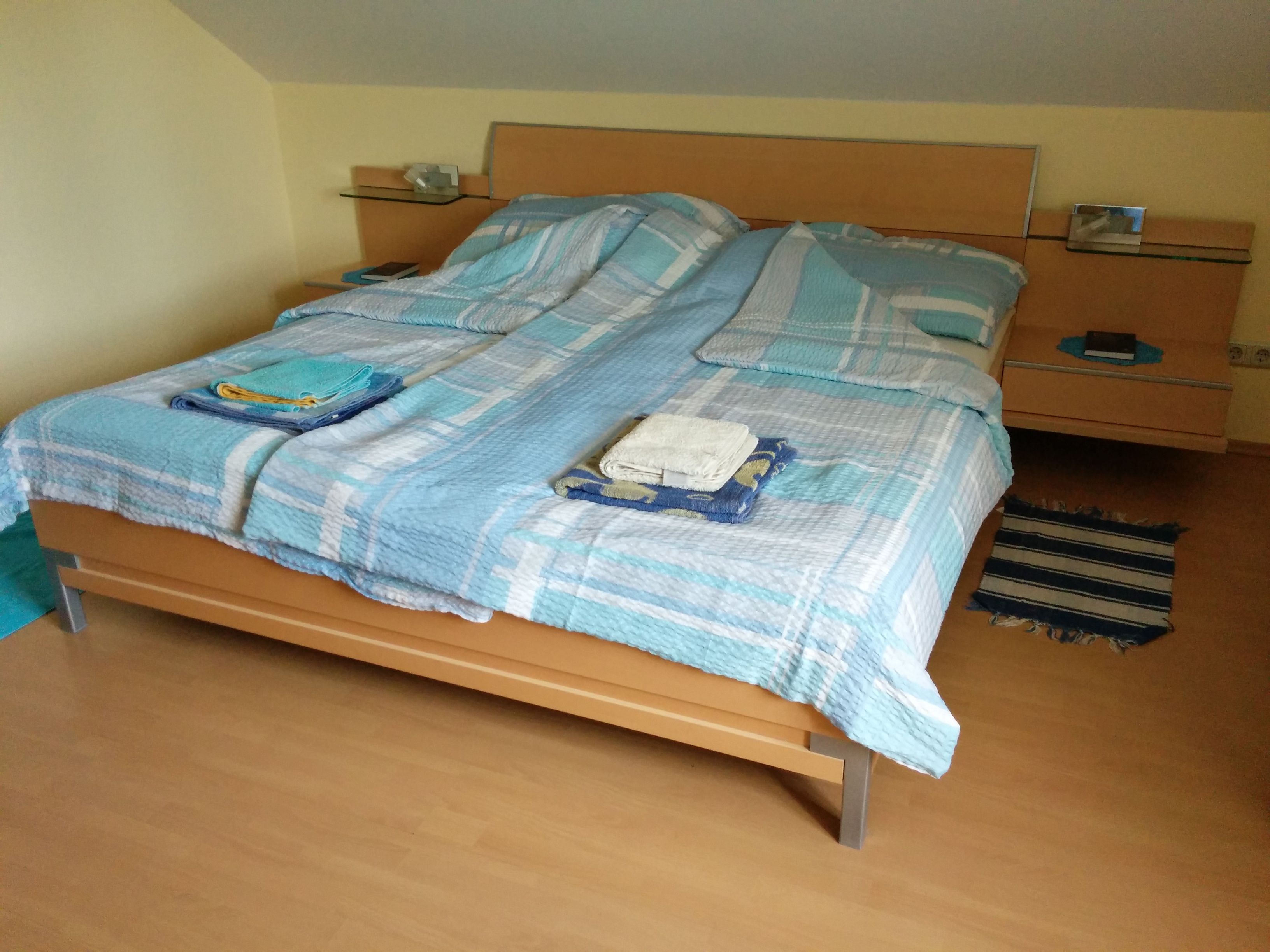 Doppelbett mit blauer Bettwäsche in einem Zimmer mit Holzboden.