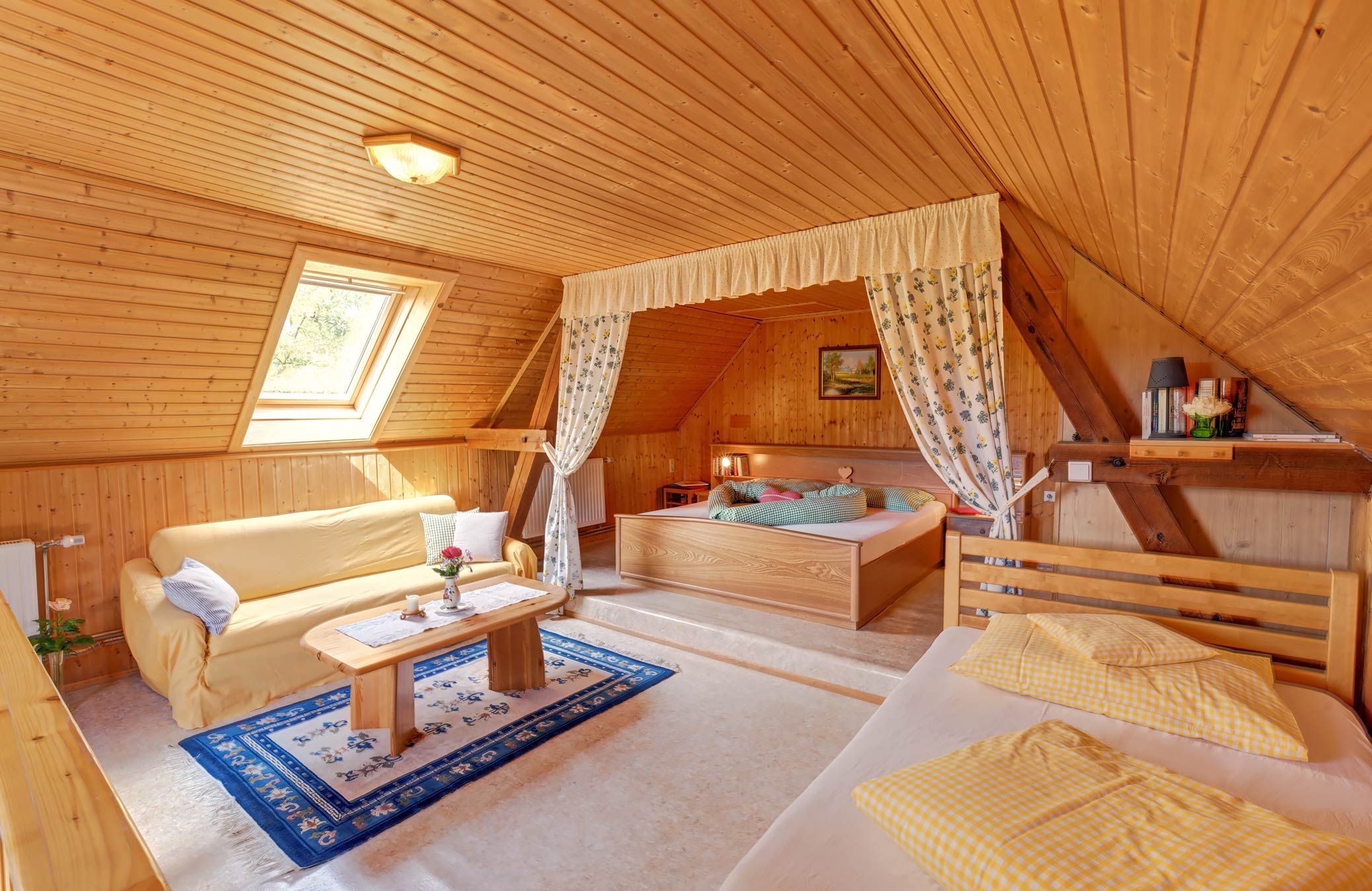 Gemütliches Schlafzimmer mit Holzwänden, einem Bett, Sofa und Dachfenster.