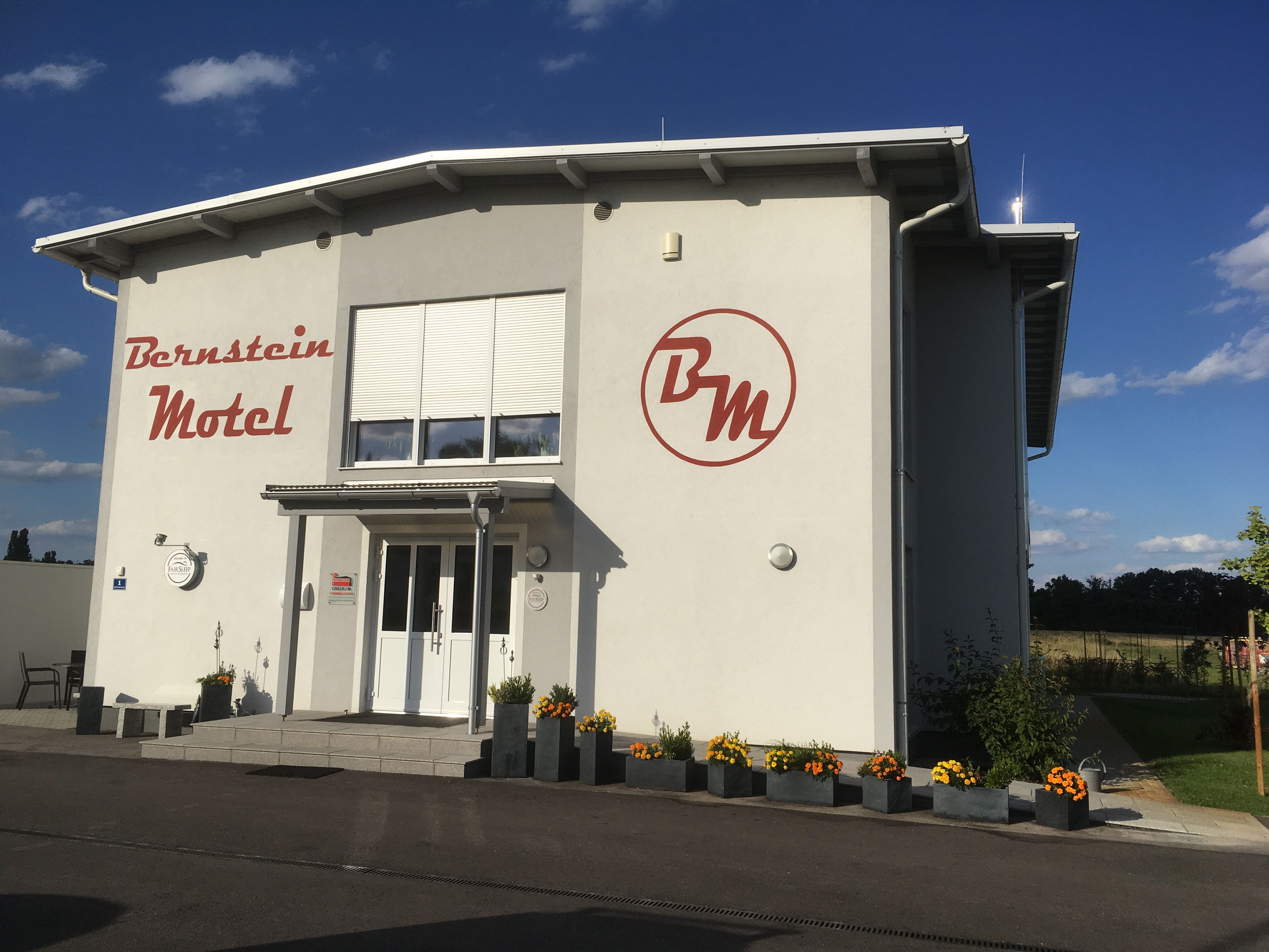 Außenansicht des Bernstein Motels mit Blumen und blauem Himmel.