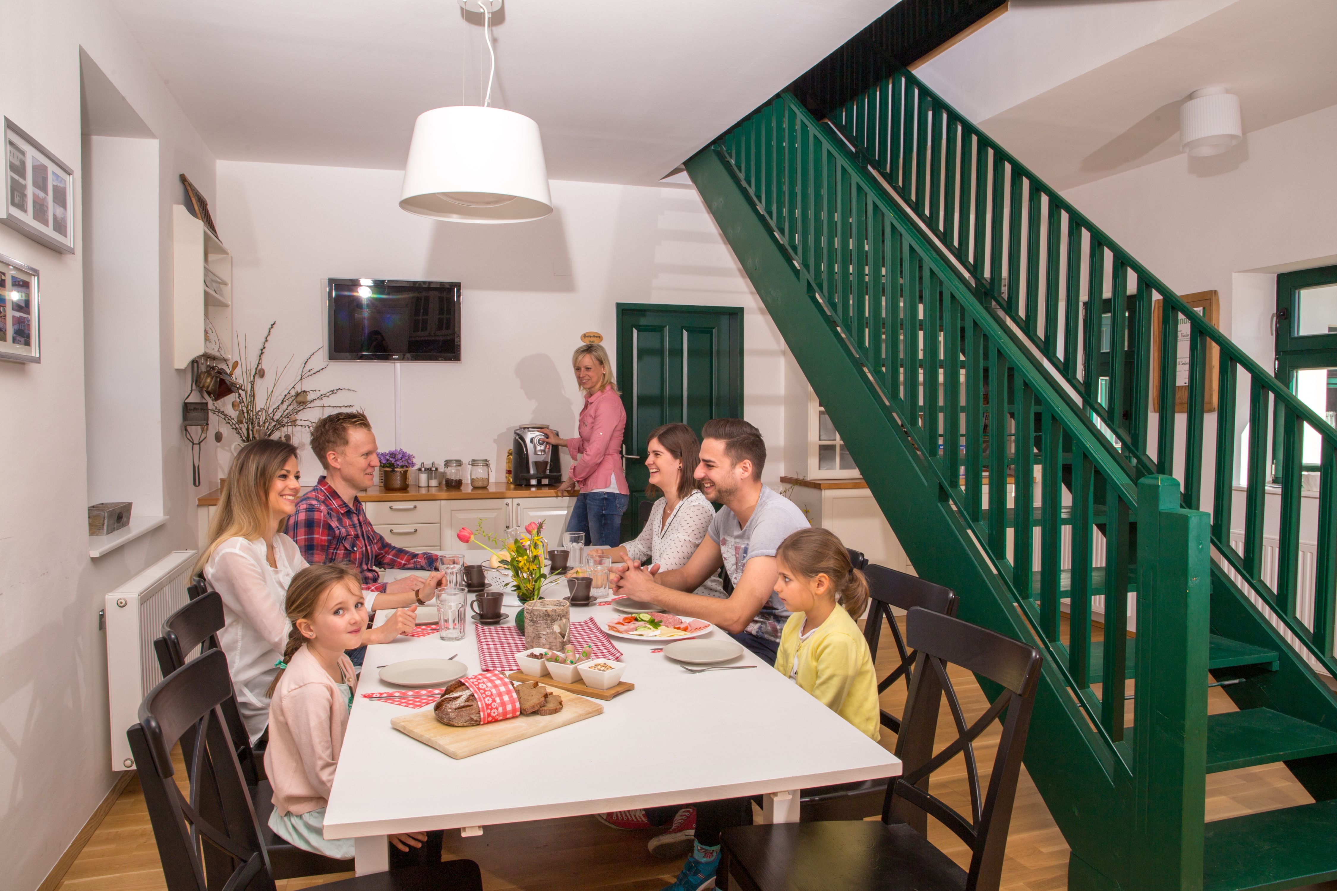 Eine Familie sitzt an einem Esstisch in einem modernen Raum mit grüner Treppe.
