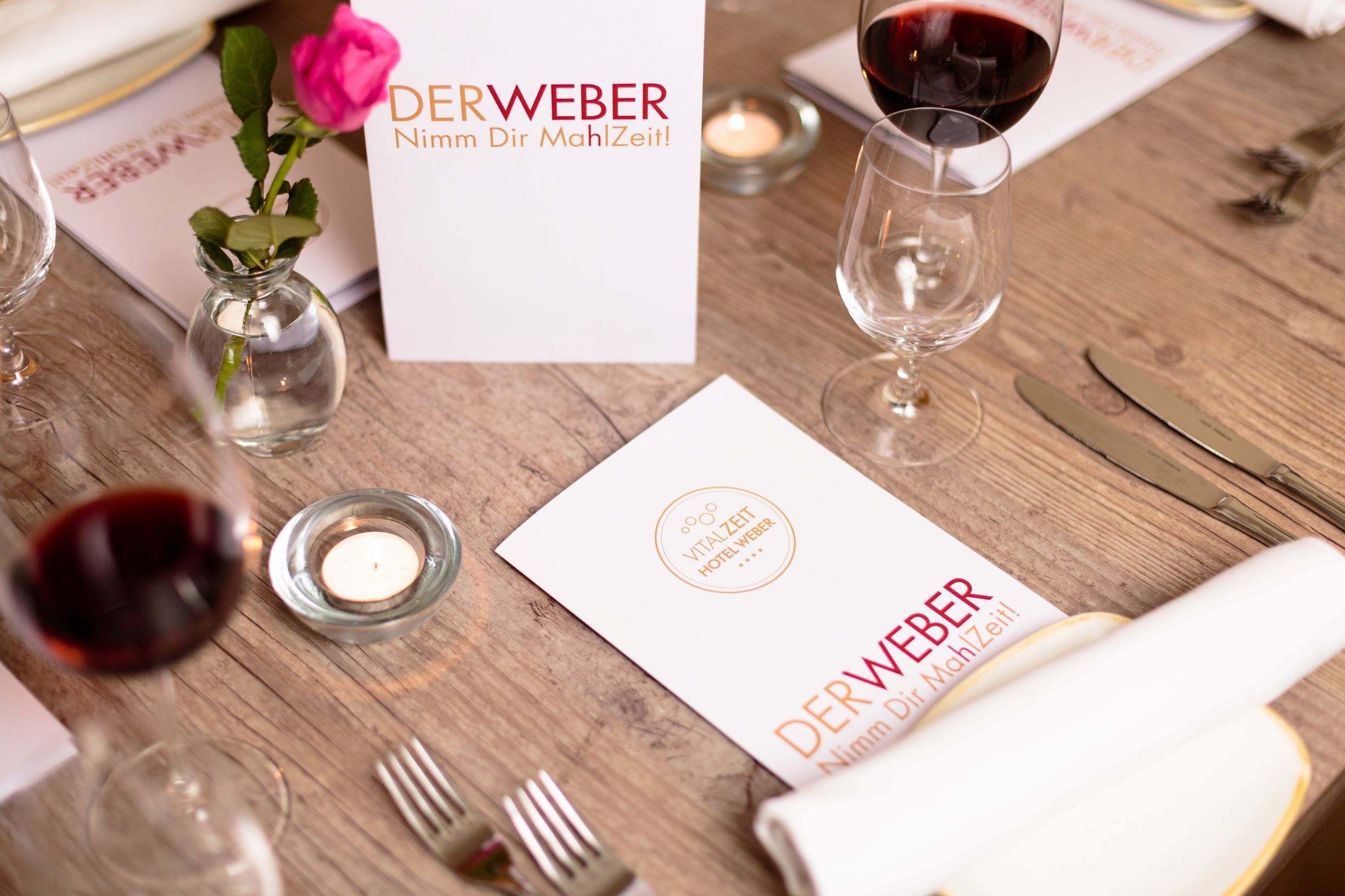Gedeckter Tisch im Restaurant Der Weber mit Menükarten, Weingläsern und einer Rose.
