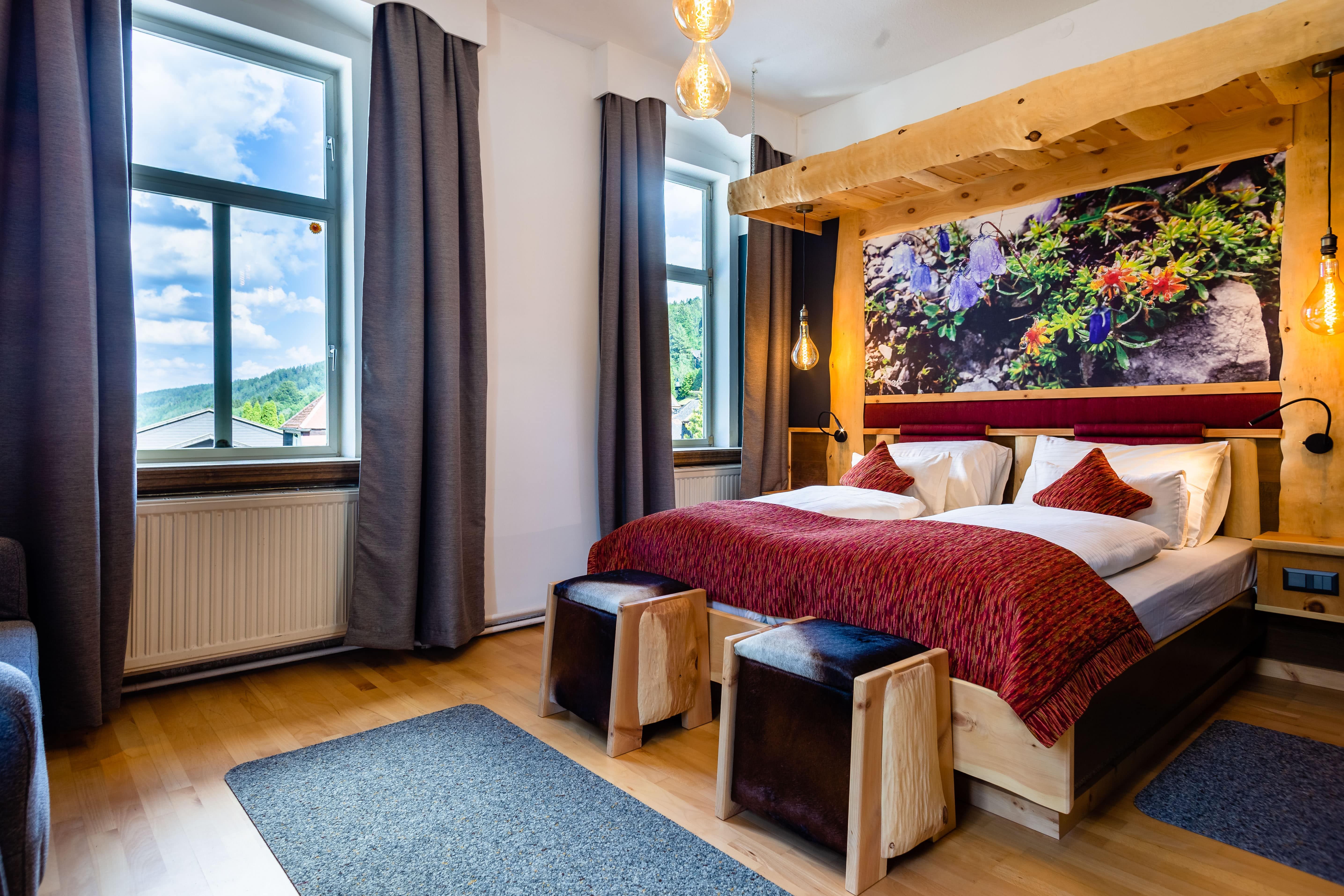 Gemütliches Hotelzimmer mit Doppelbett, Holzmöbeln und großem Fenster mit Blick auf die Natur.