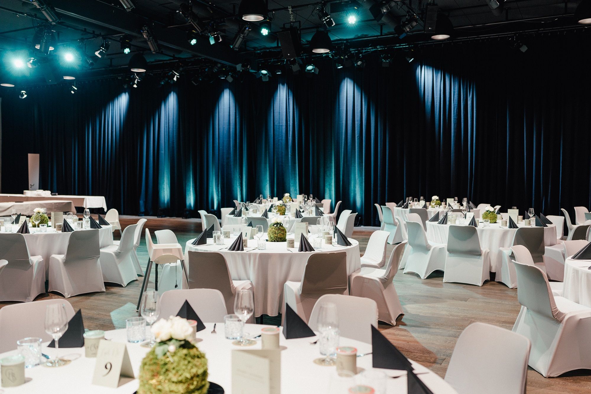 Elegante Galabestuhlung mit runden Tischen, weißen Tischdecken und schwarzen Servietten in einem festlich beleuchteten Saal.