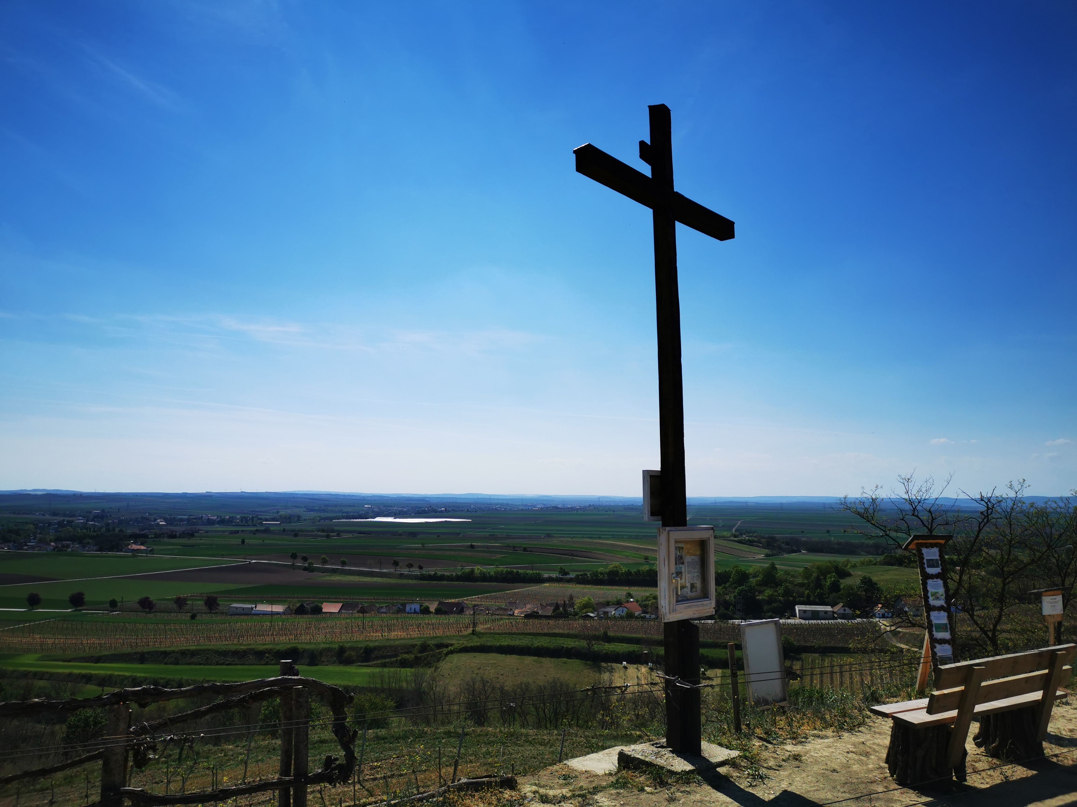 Ein großes Holzkreuz auf einem Hügel mit Blick auf eine weite Landschaft unter blauem Himmel.