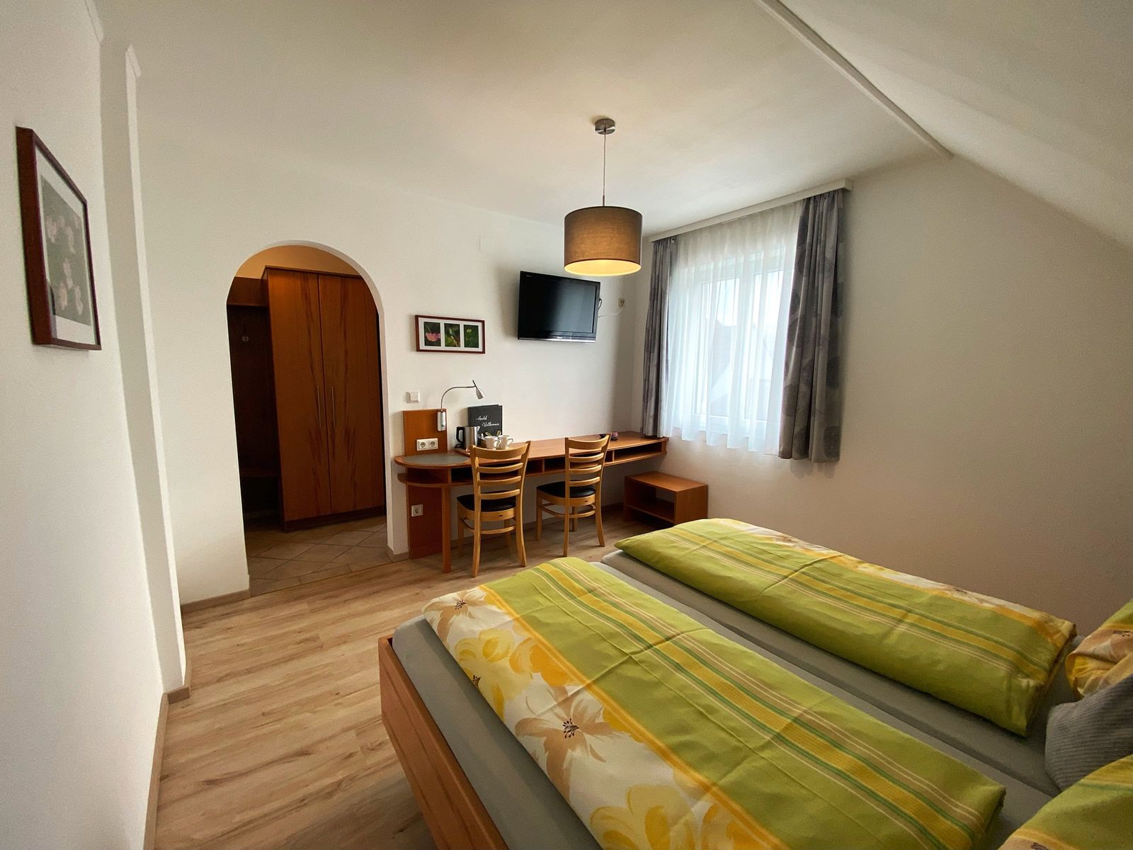 Ein gemütliches Doppelzimmer mit zwei Betten, Schreibtisch, Stühlen und einem Fernseher an der Wand.