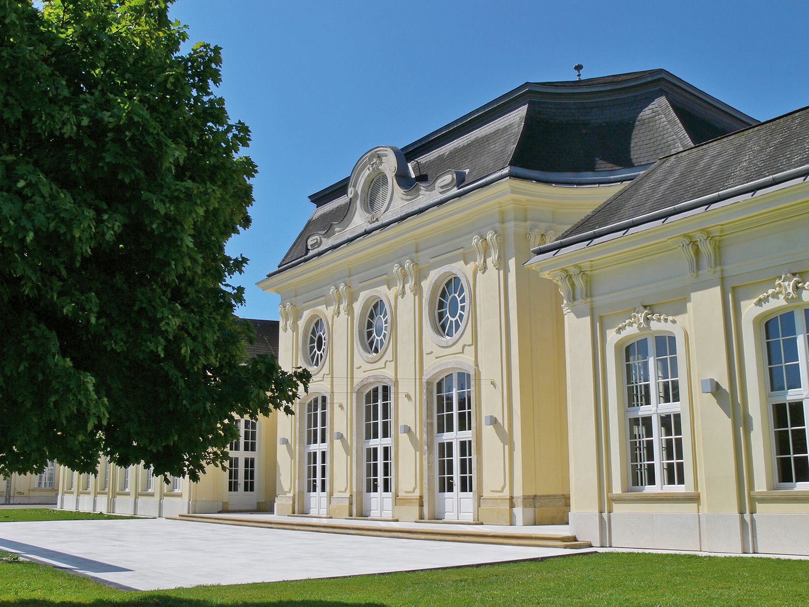 Historisches Gebäude mit gelber Fassade und großen Fenstern im Sonnenschein.