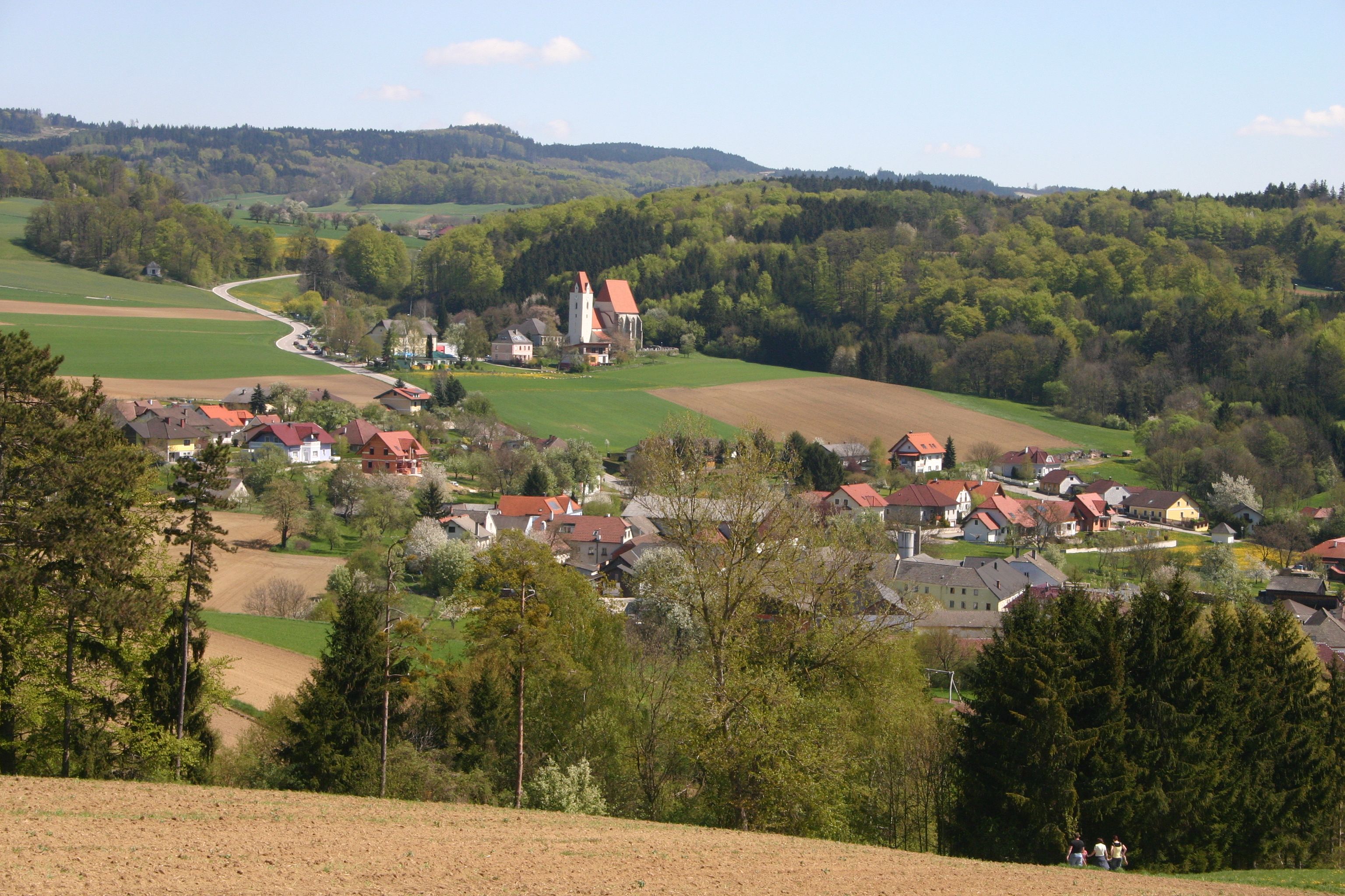 Landschaft mit Dorf, Kirche und Hügeln im Hintergrund.