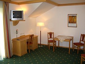 Hotelzimmer mit grünem Teppich, Holzmöbeln, Tisch, Stühlen und Fernseher.