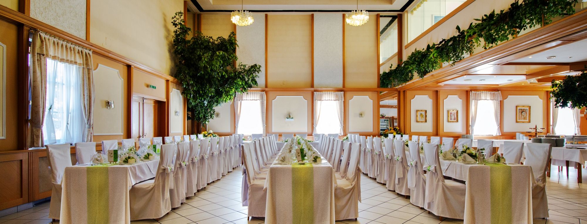 Eleganter Bankettsaal mit gedeckten Tischen und weißen Stühlen, dekoriert mit Pflanzen und Kronleuchtern.