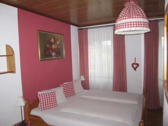 Schlafzimmer mit rot-weiß karierten Vorhängen und Bettwäsche.