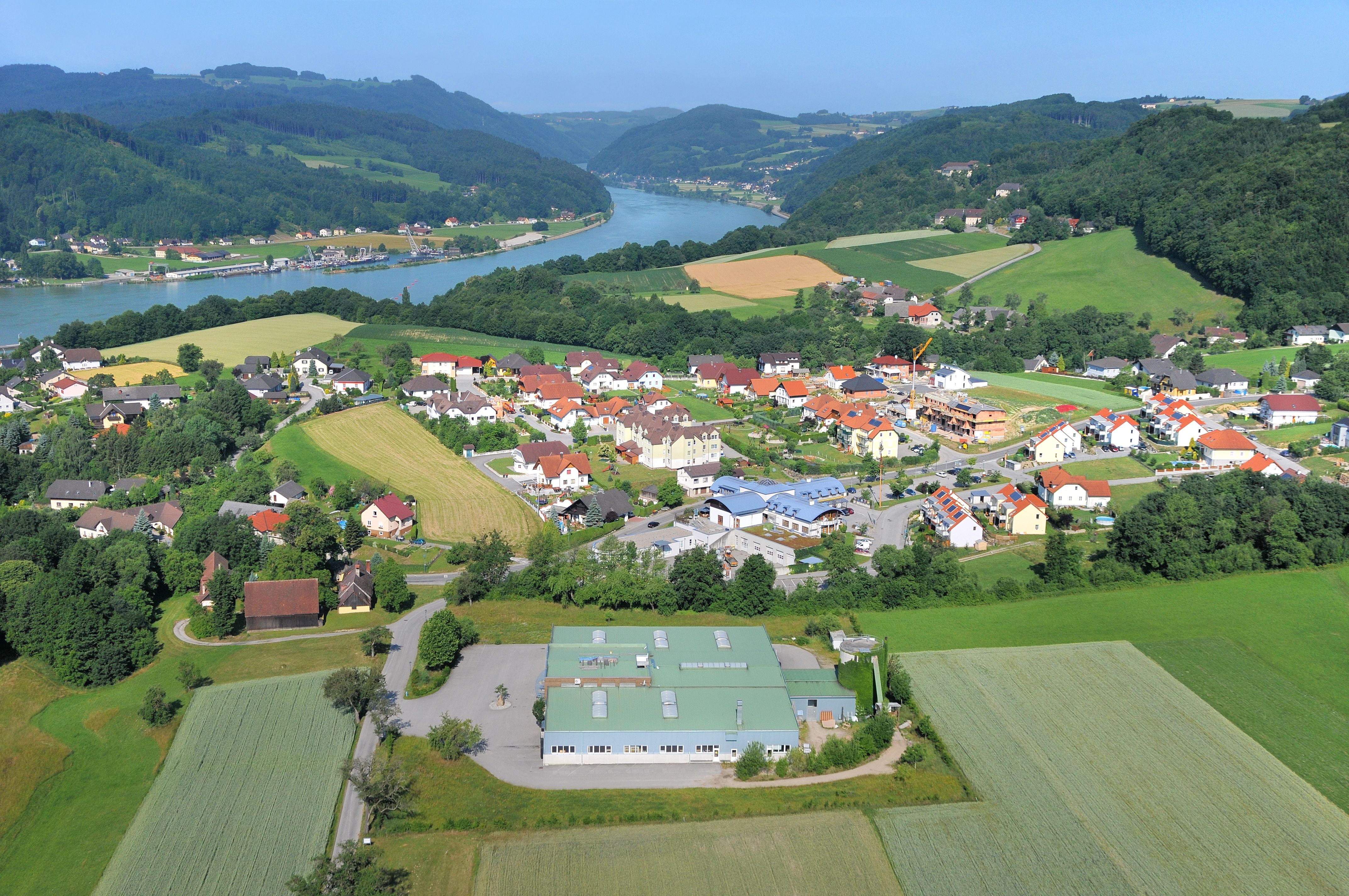 Luftaufnahme eines Dorfes im Donautal mit Fluss und Hügeln im Hintergrund.