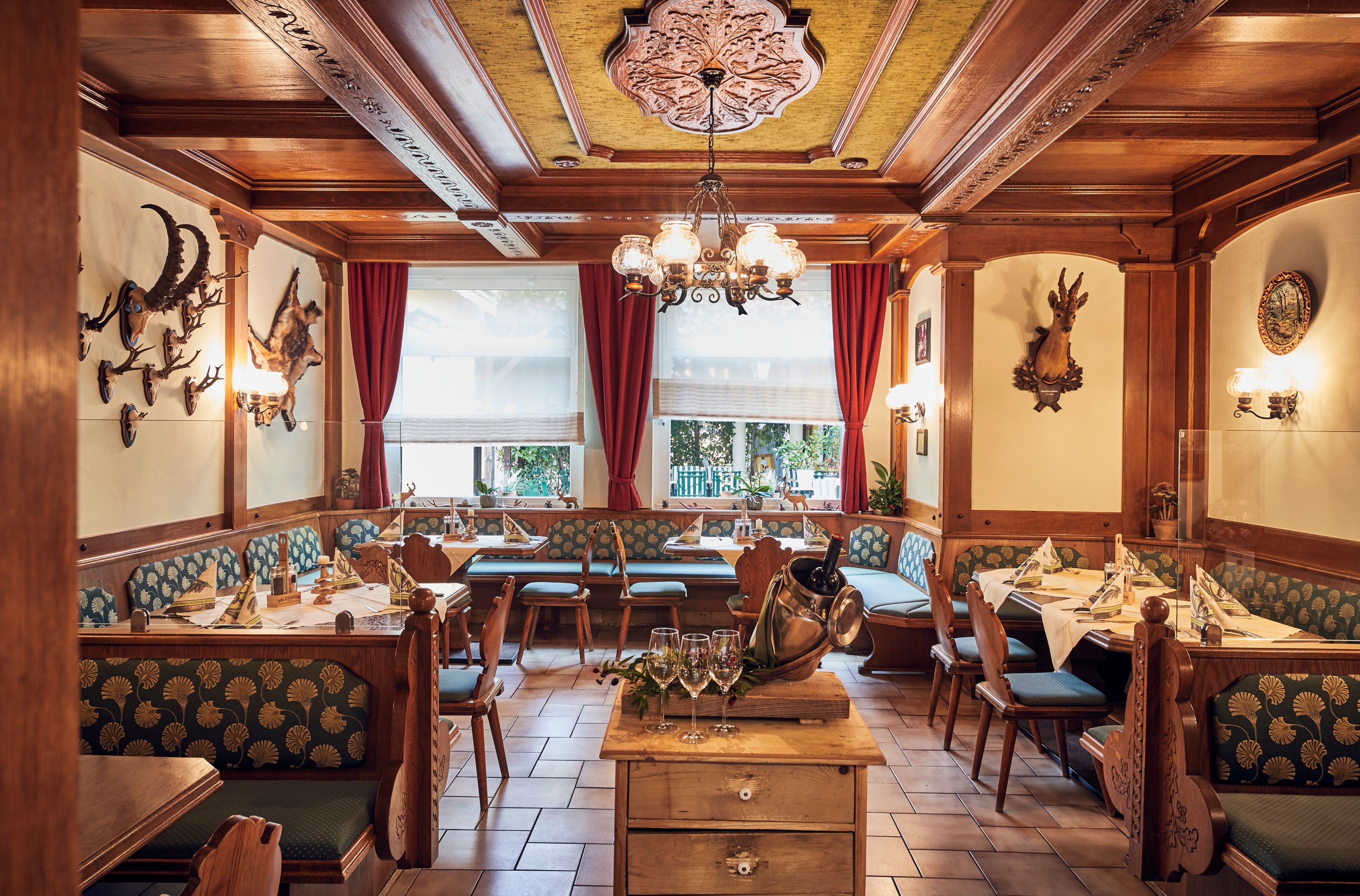 Gemütliche Jägerstube mit Holzmöbeln, Jagdtrophäen an den Wänden und gedeckten Tischen.