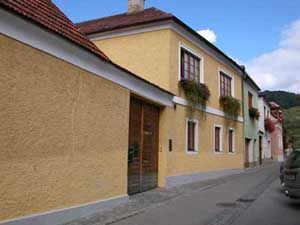Gelbes Haus mit roten Dachziegeln und Blumenkästen an den Fenstern in einer schmalen Straße.