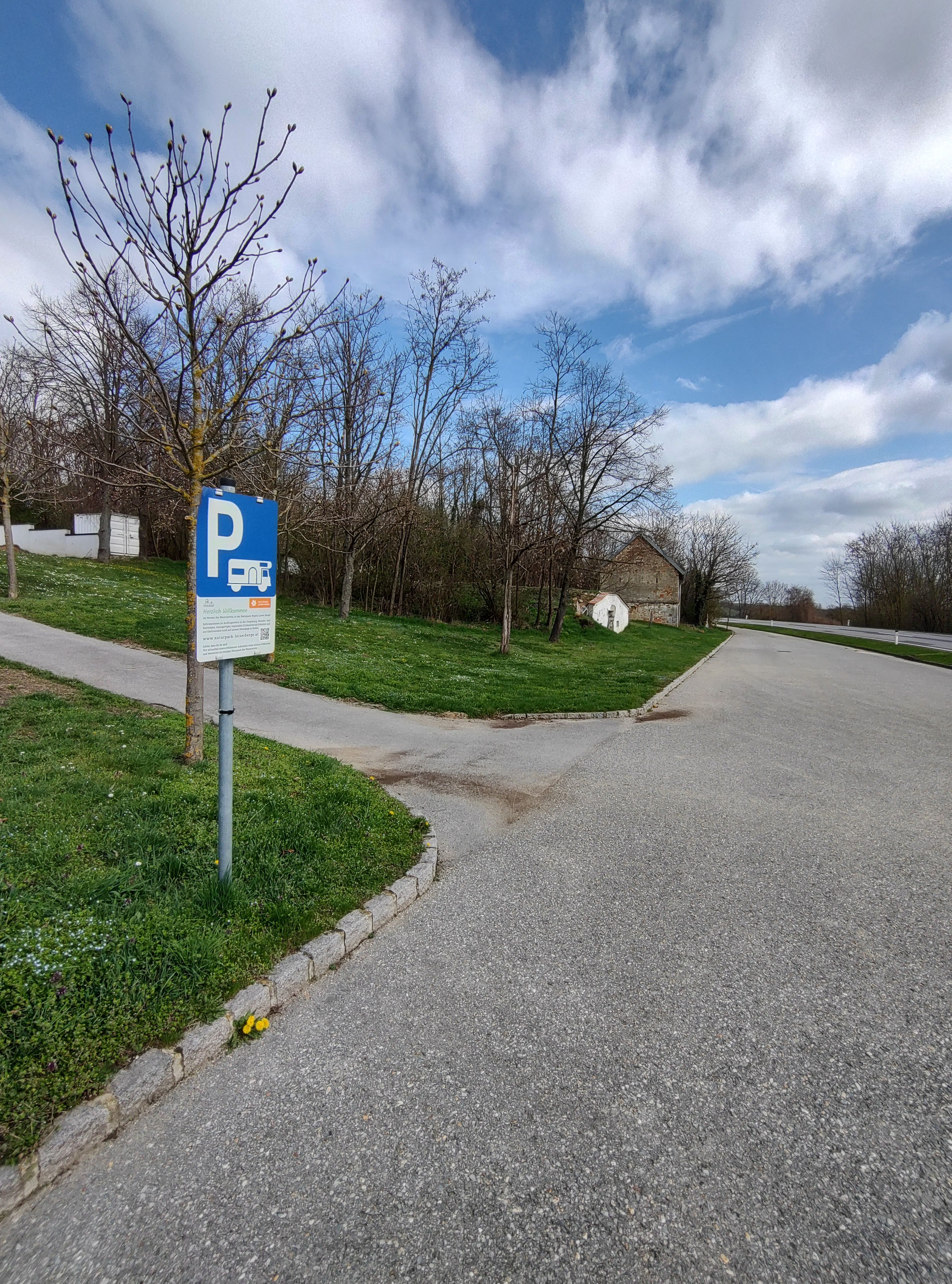 Wohnmobilstellplatz mit Parkplatzschild und Bäumen im Hintergrund.