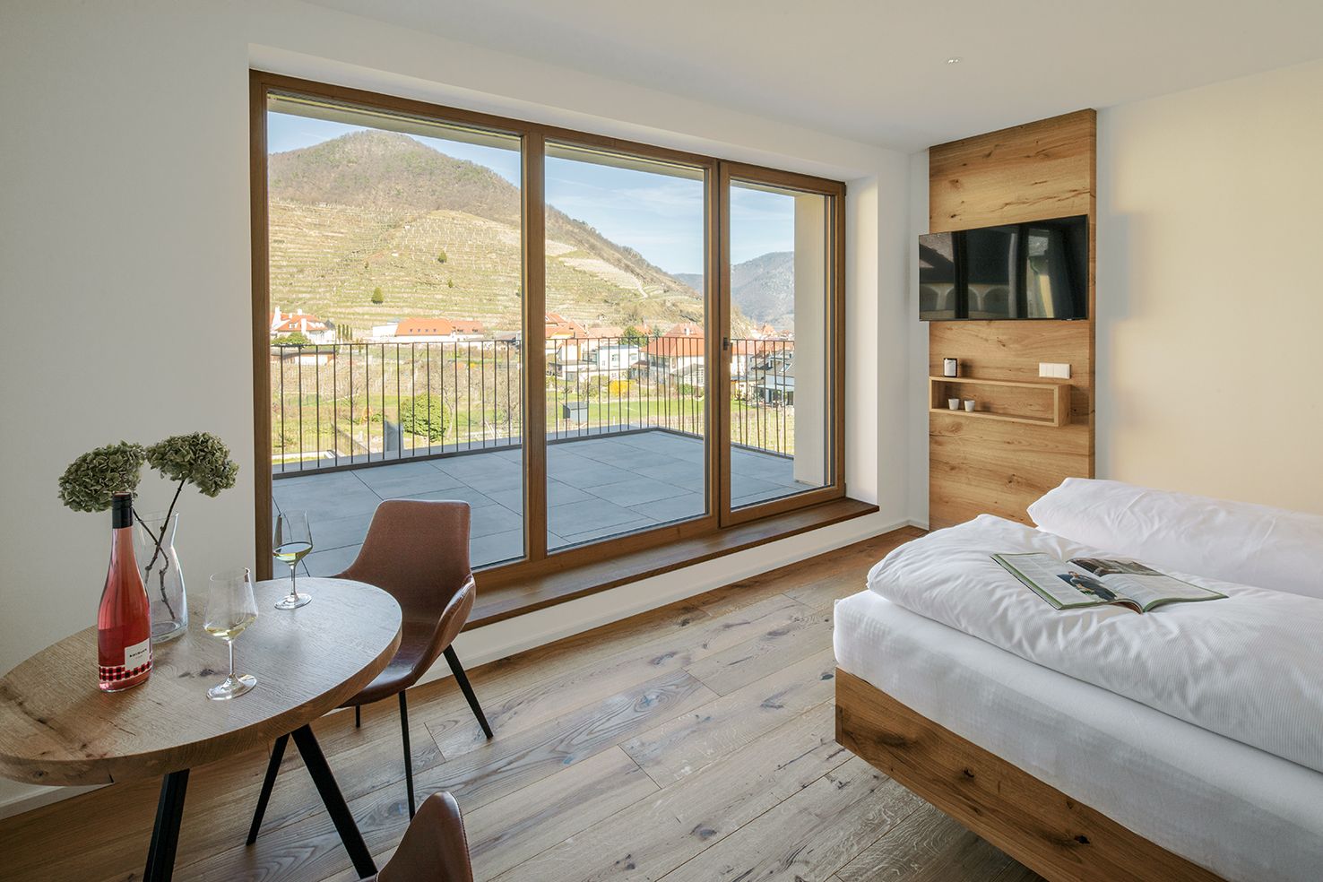 Innenansicht einer Ferienwohnung mit Blick auf Weinberge durch große Fenster.