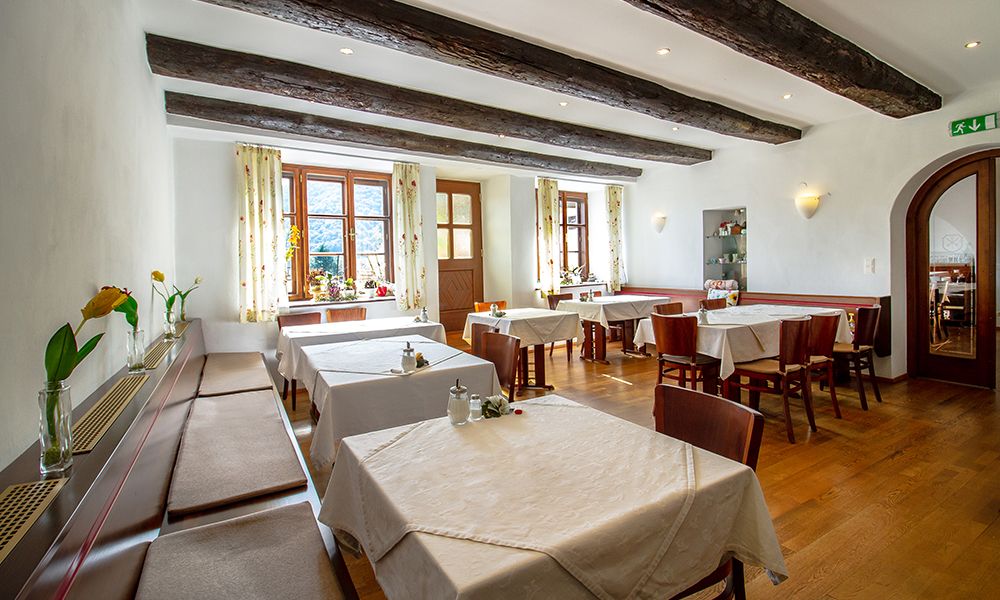 Ein gemütlicher Frühstücksraum mit Holzbalken, gedeckten Tischen und Blumen auf den Fensterbänken.