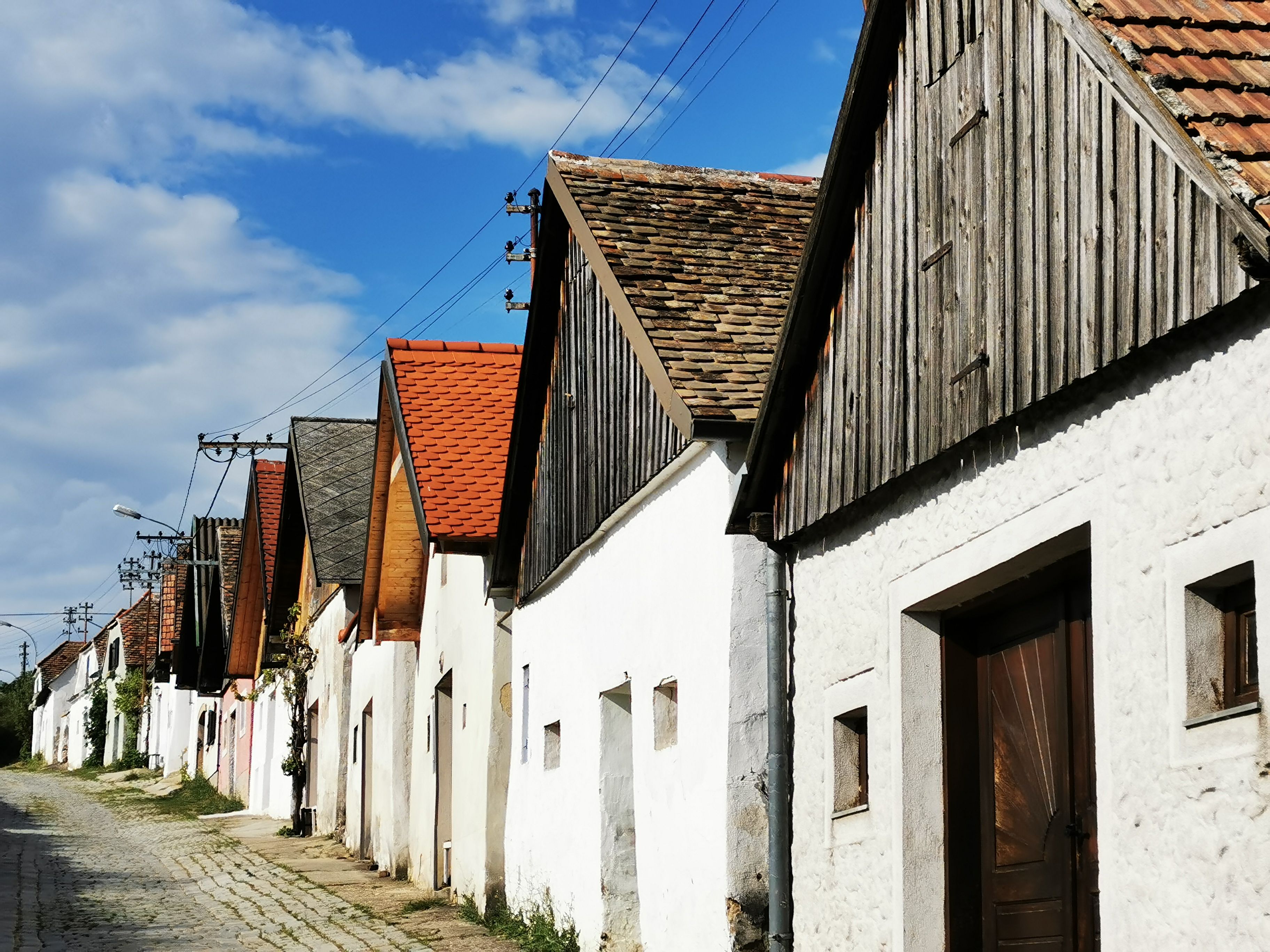 Reihe von Weinkellern in Haugsdorf mit roten und grauen Dächern unter blauem Himmel.