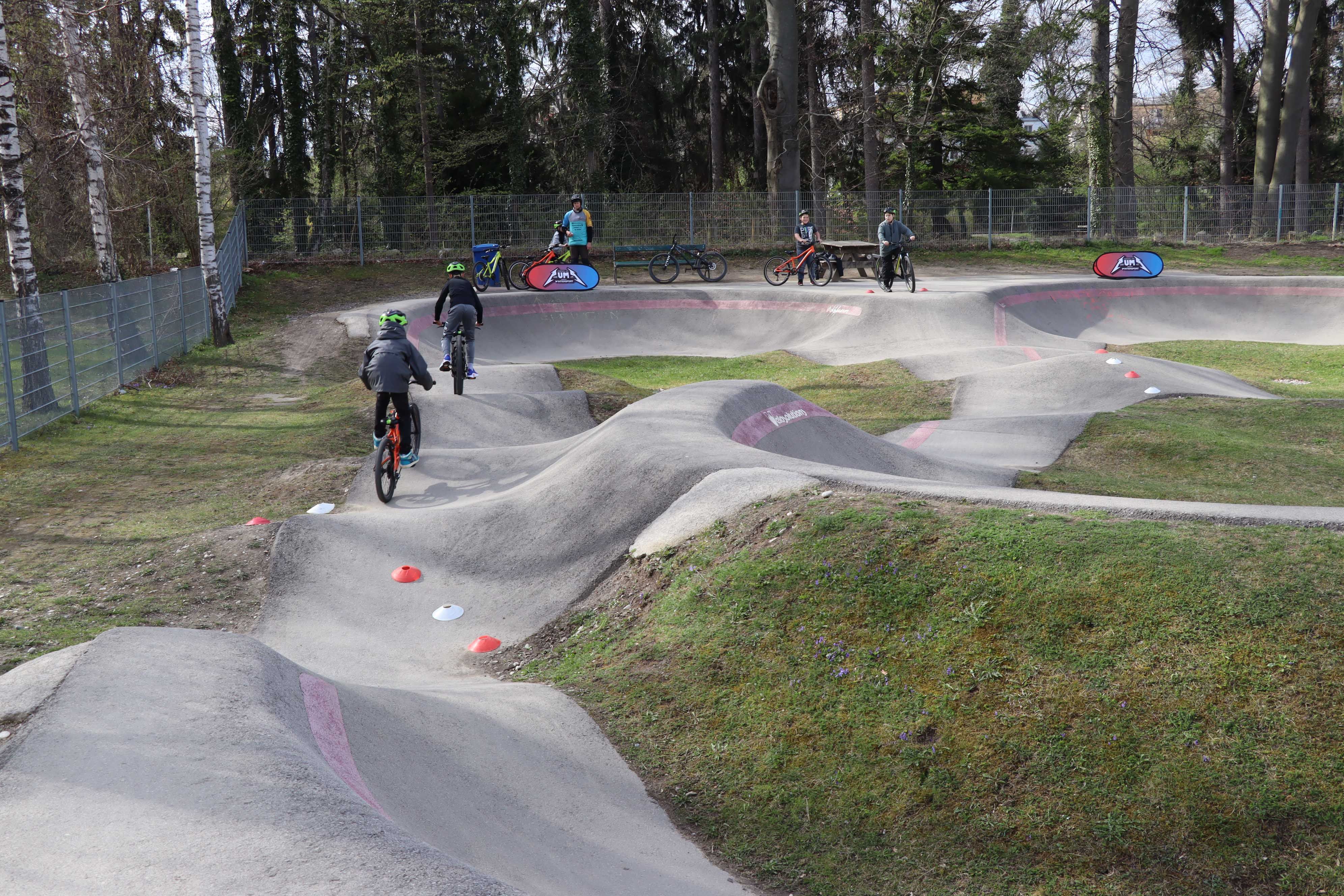 Kinder fahren mit Fahrrädern auf einem Pumptrack.