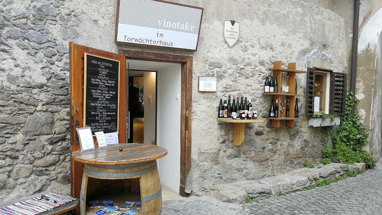 Eingang zu einem Weinladen in einem alten Steingebäude mit Weinfässern und Weinflaschen an der Wand.