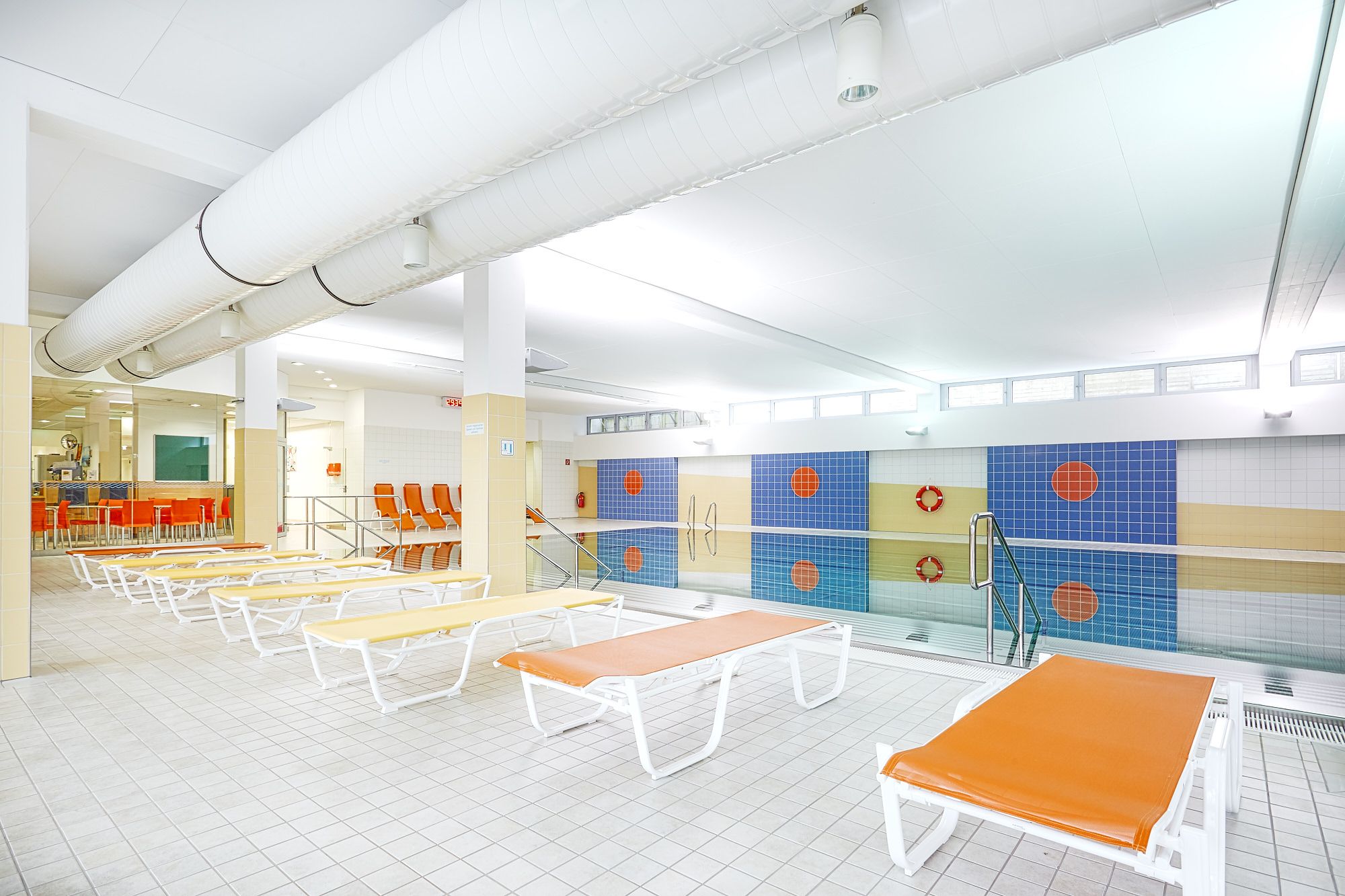 Innenansicht eines Hallenbads mit Liegestühlen und Schwimmbecken.