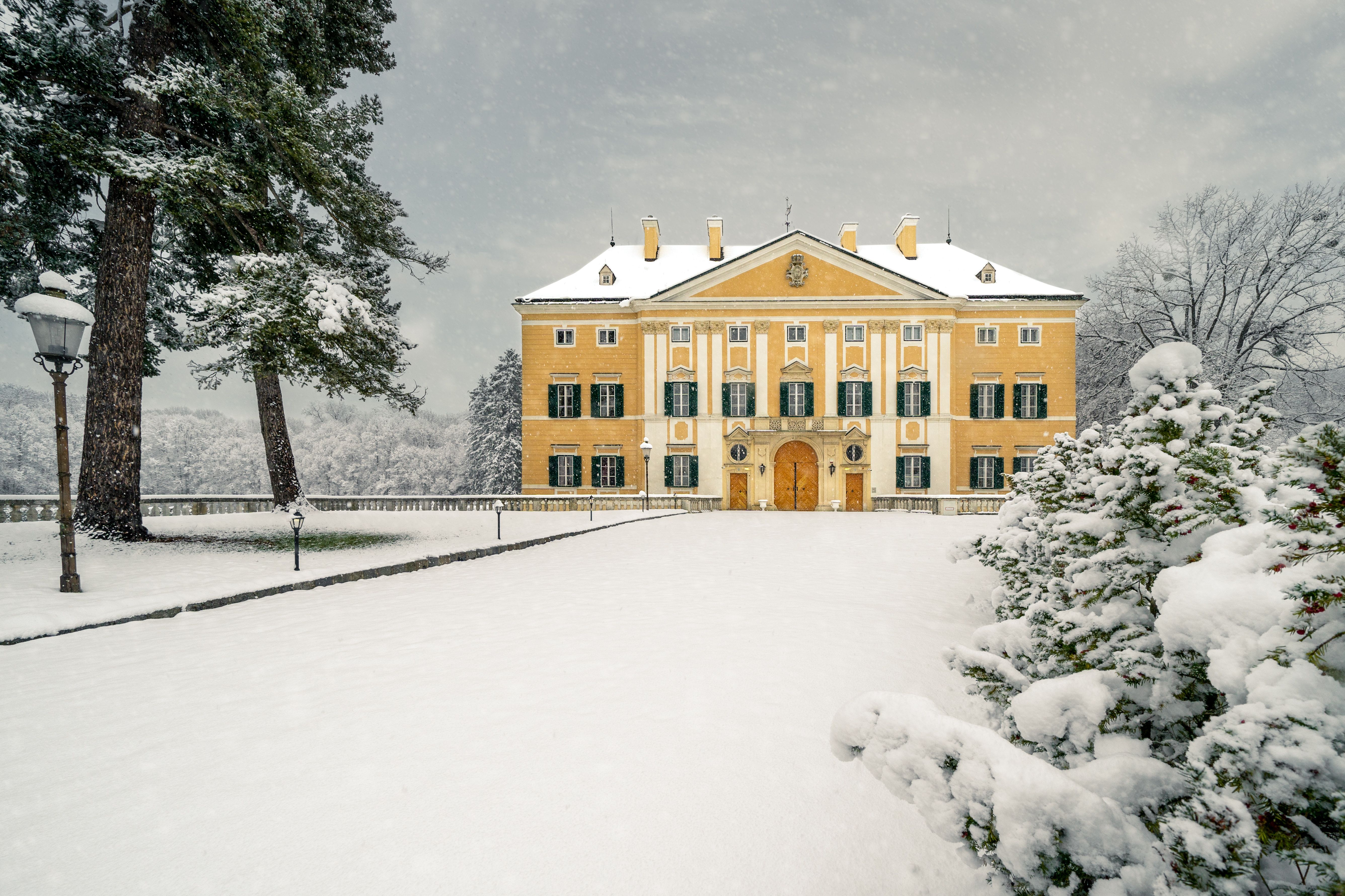 Schloss Frohsdorf mit vielen Fenstern und gelber Fassade im Winter mit Schnee bedeckt.
