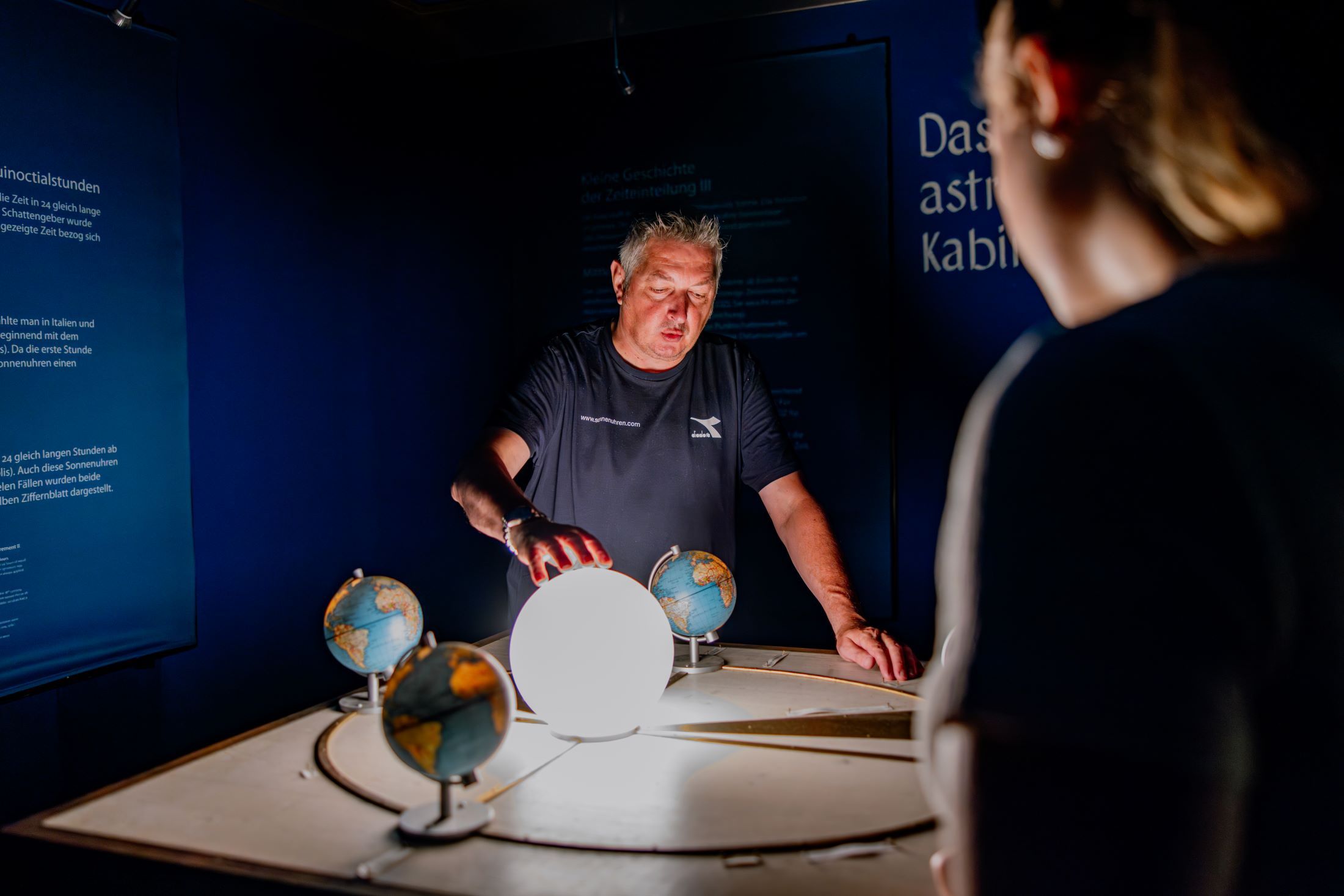 Ein Mann erklärt anhand eines Modells den Sonnenlauf in einem dunklen Raum.