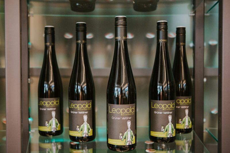 Fünf Flaschen Grüner Veltliner Wein der Marke Leopold in einem Regal.