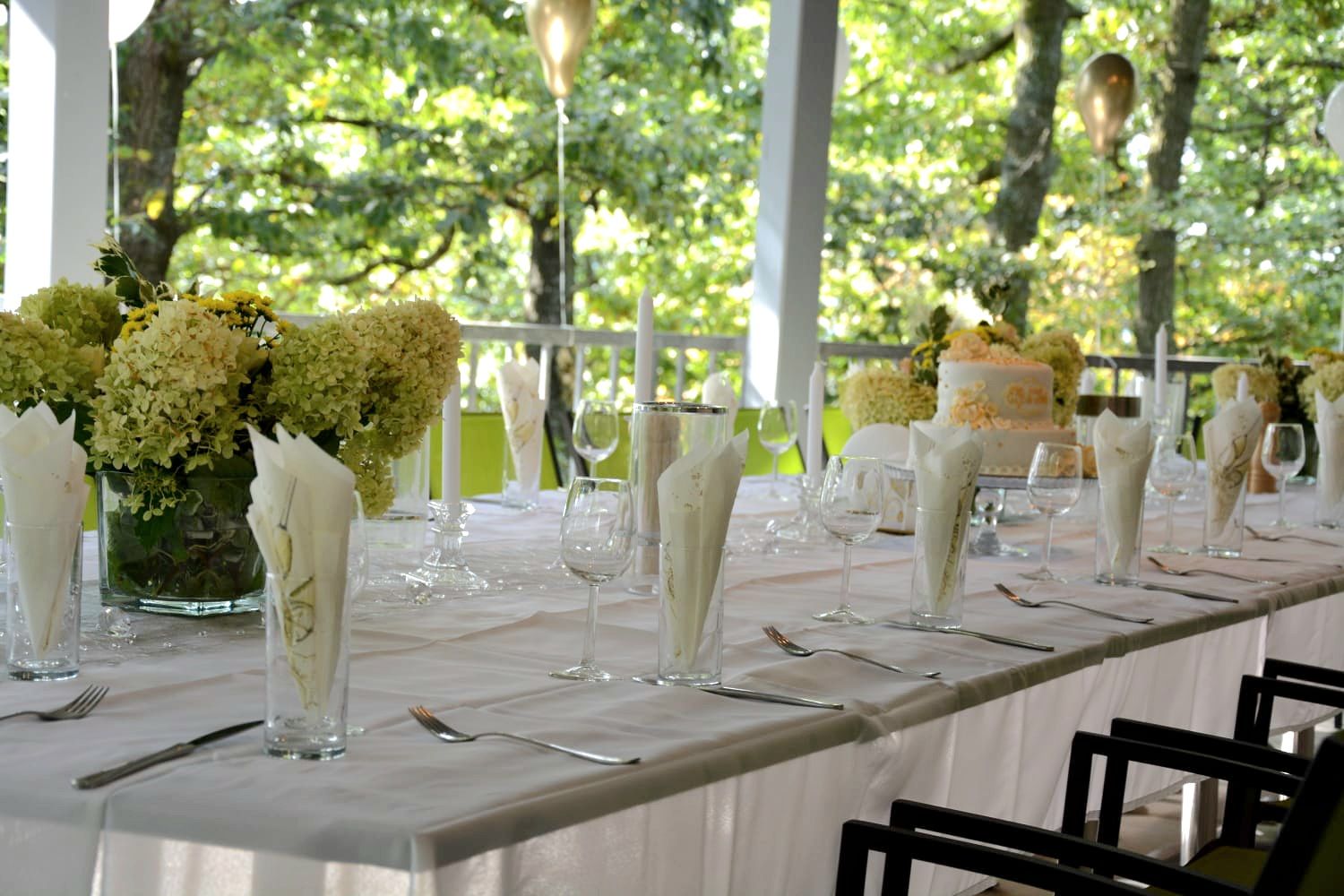 Feierlich gedeckter Tisch in weiß auf einer Terasse mit Blumen und Kerzen.